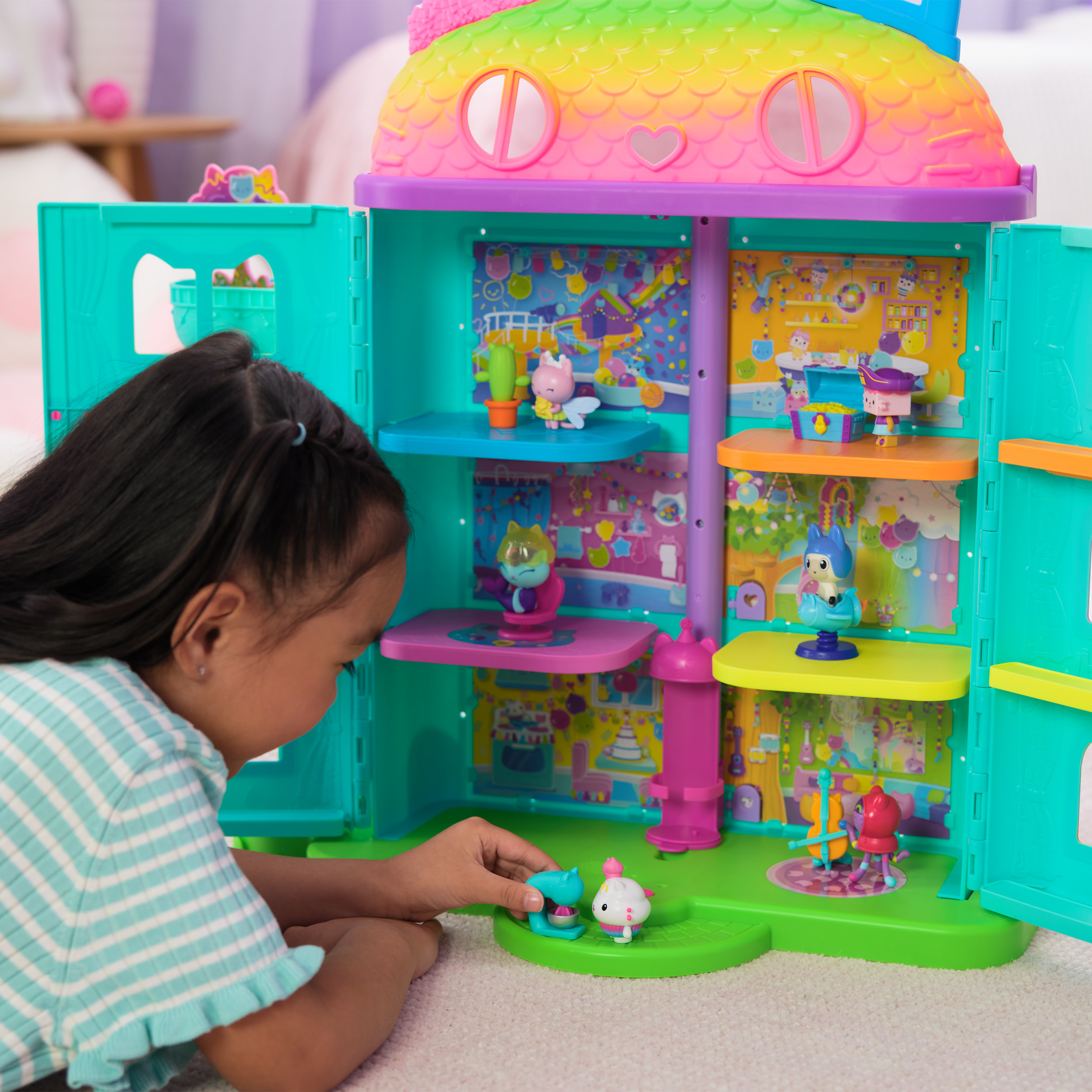 Una niña mira una casa de muñecas de juguete. Es colorida con múltiples habitaciones y figuras.