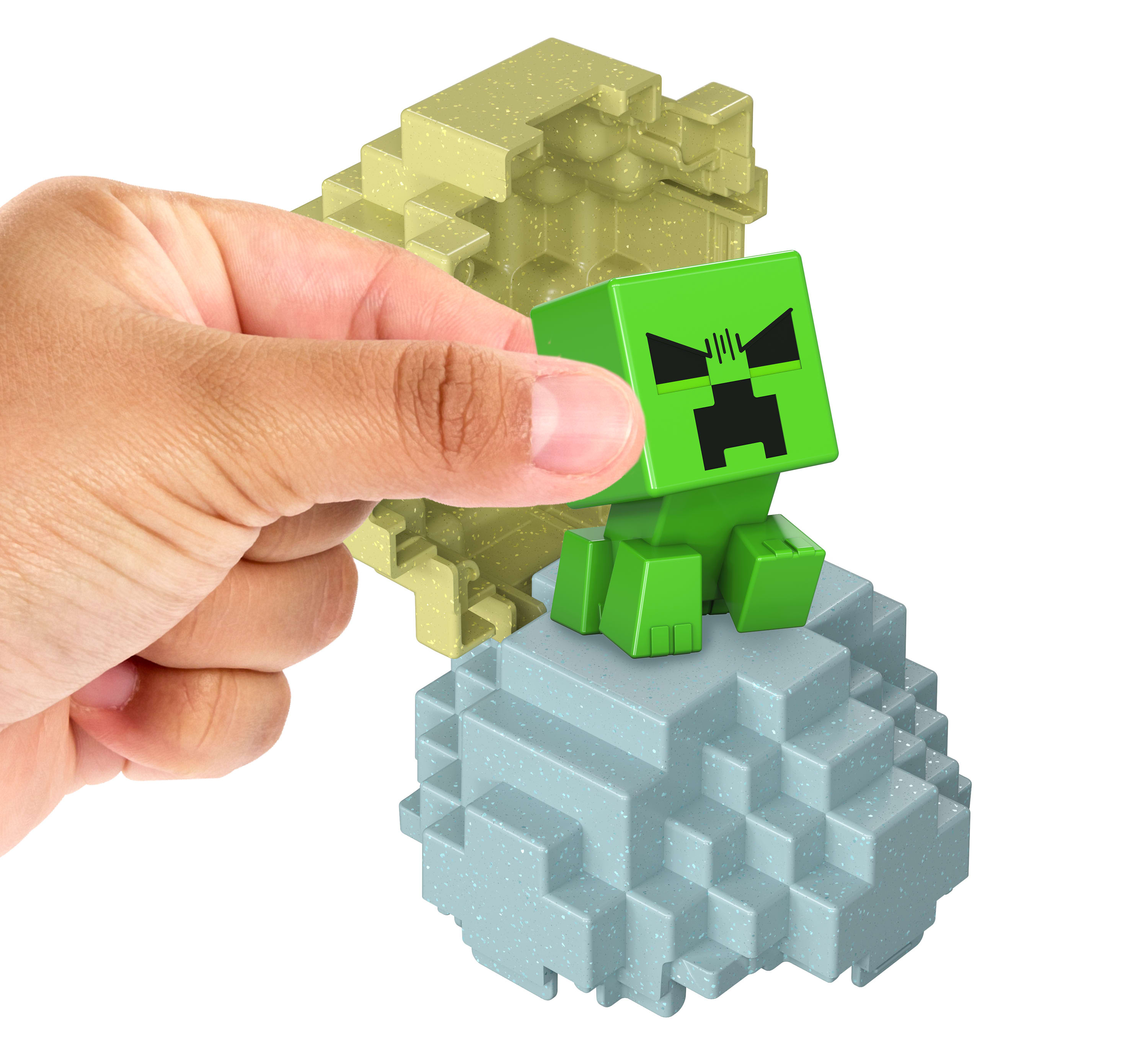 Dłoń trzymająca zieloną figurkę Creepera na zestawie klocków z motywem Minecraft.
