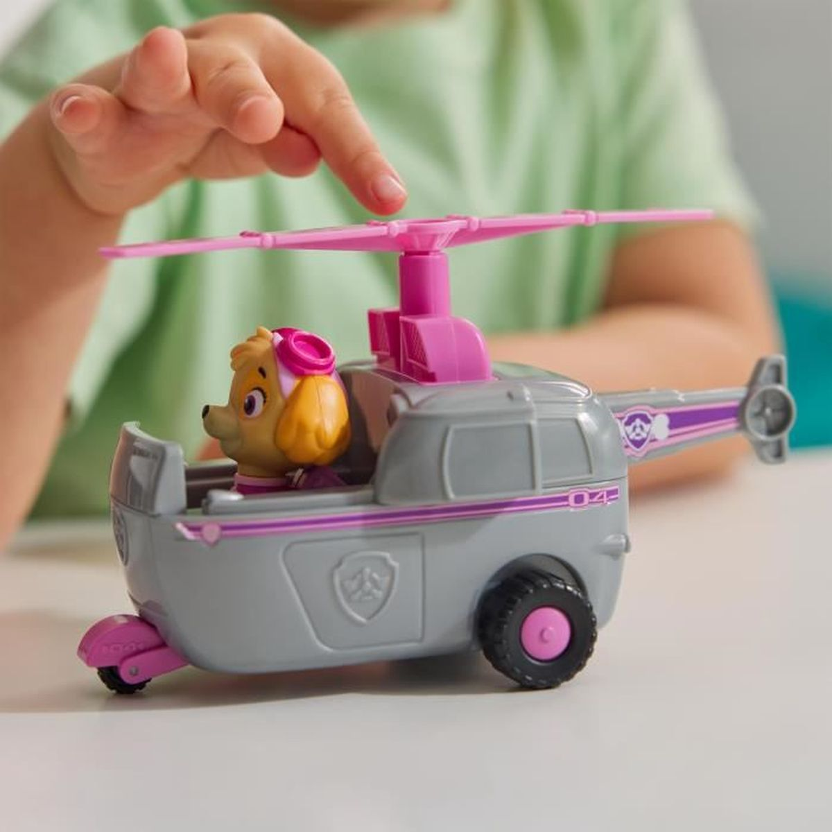 Een kinderhand die een grijze en roze speelgoedhelikopter aanraakt. Een gele hondenspeelgoed zit in de helikopter.