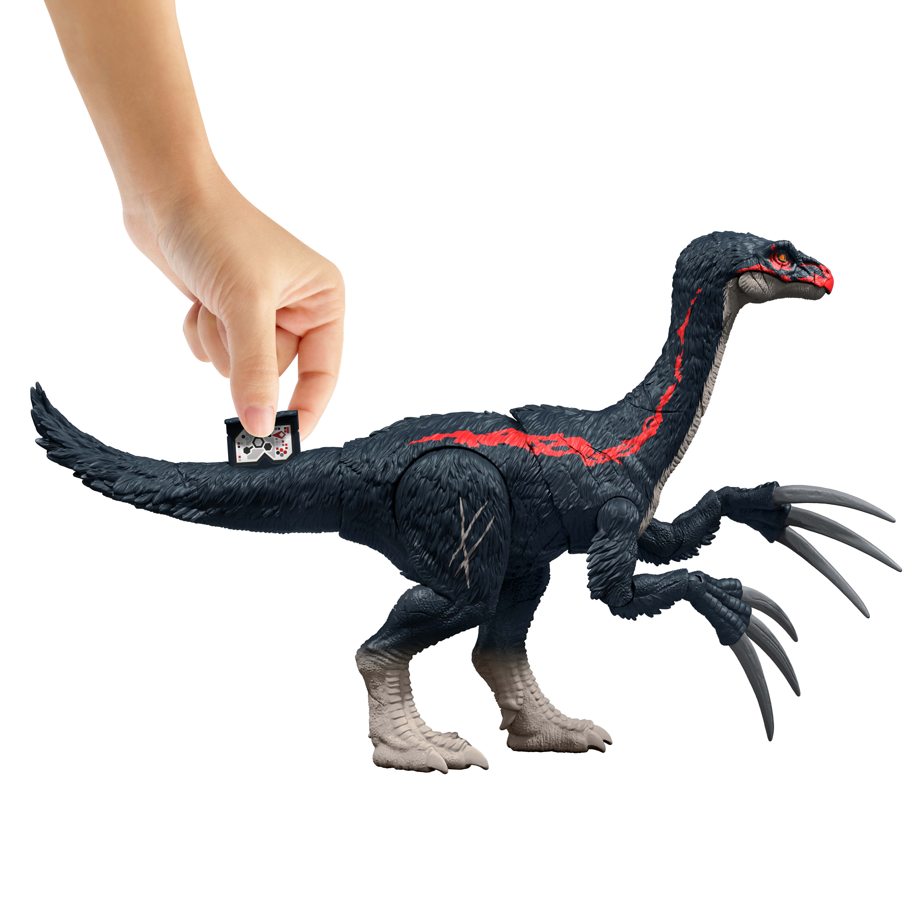 A hand is holding a small black controller near a black and red dinosaur toy.