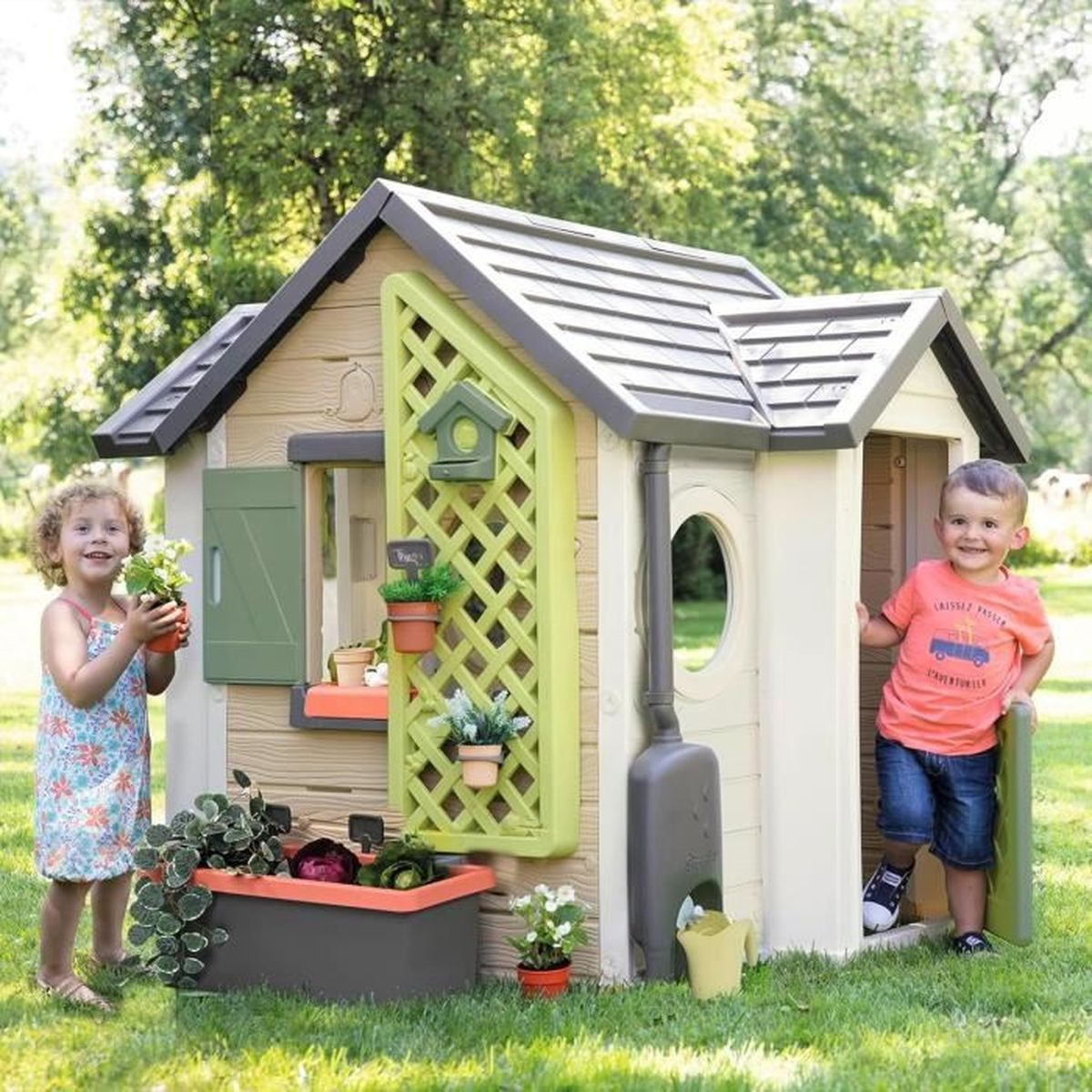 Zwei Kinder spielen in einem Garten in der Nähe eines Spielhauses. Das Spielhaus hat ein grünes Spalier und Blumenkästen.