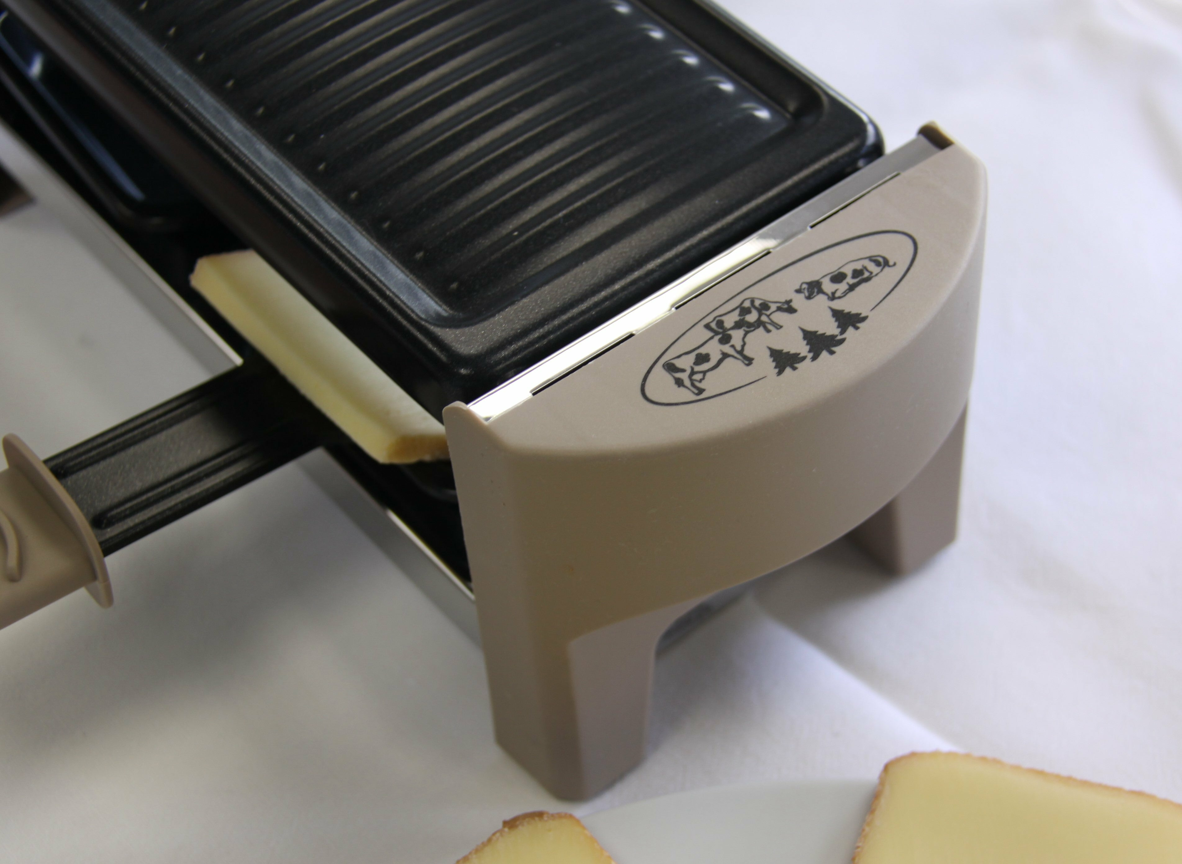 Szczegół grilla do raclette: ser zeskrobany na talerz. Białe tło.