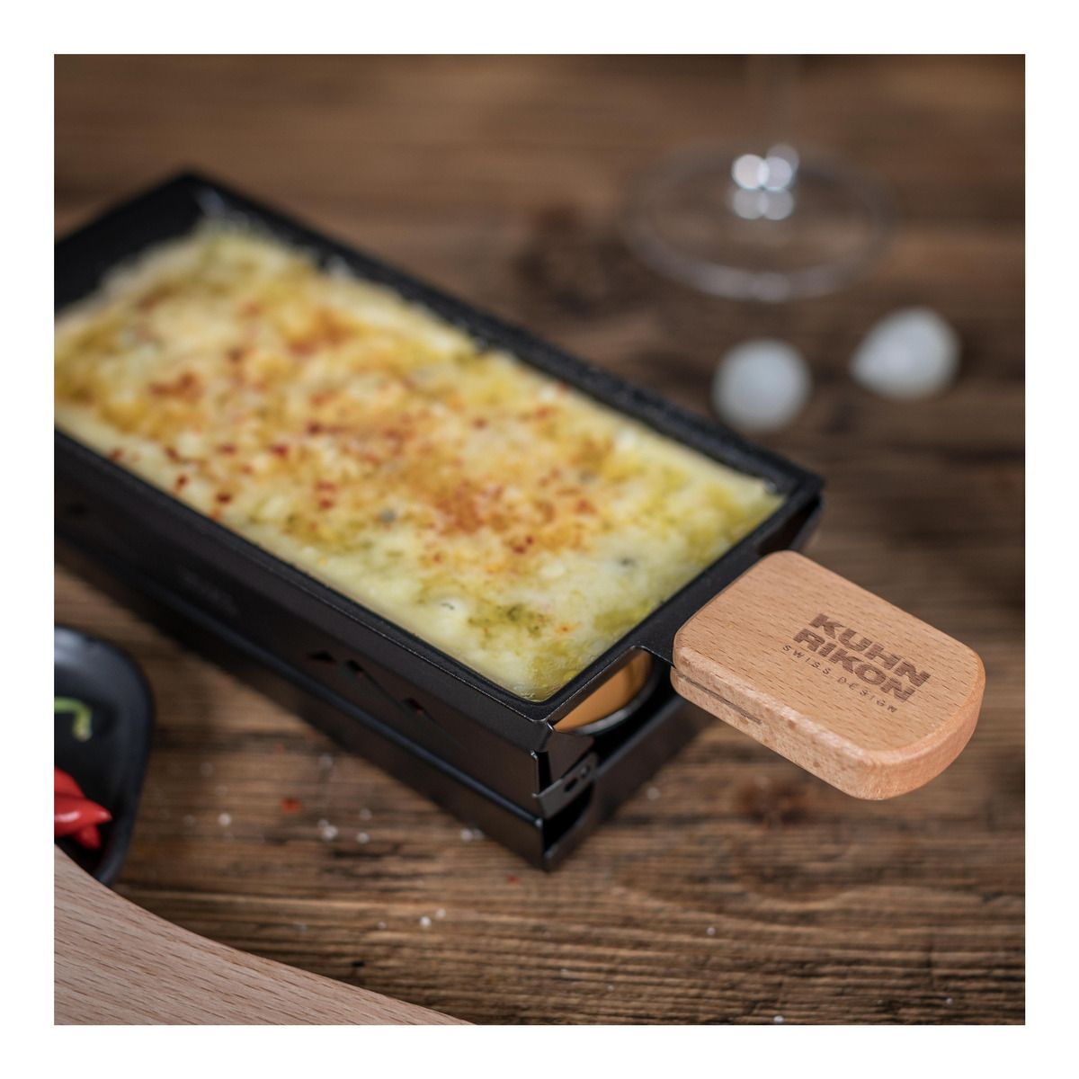 Raclette-Grill mit geschmolzenem Käse, Holzgriff. Holztisch.