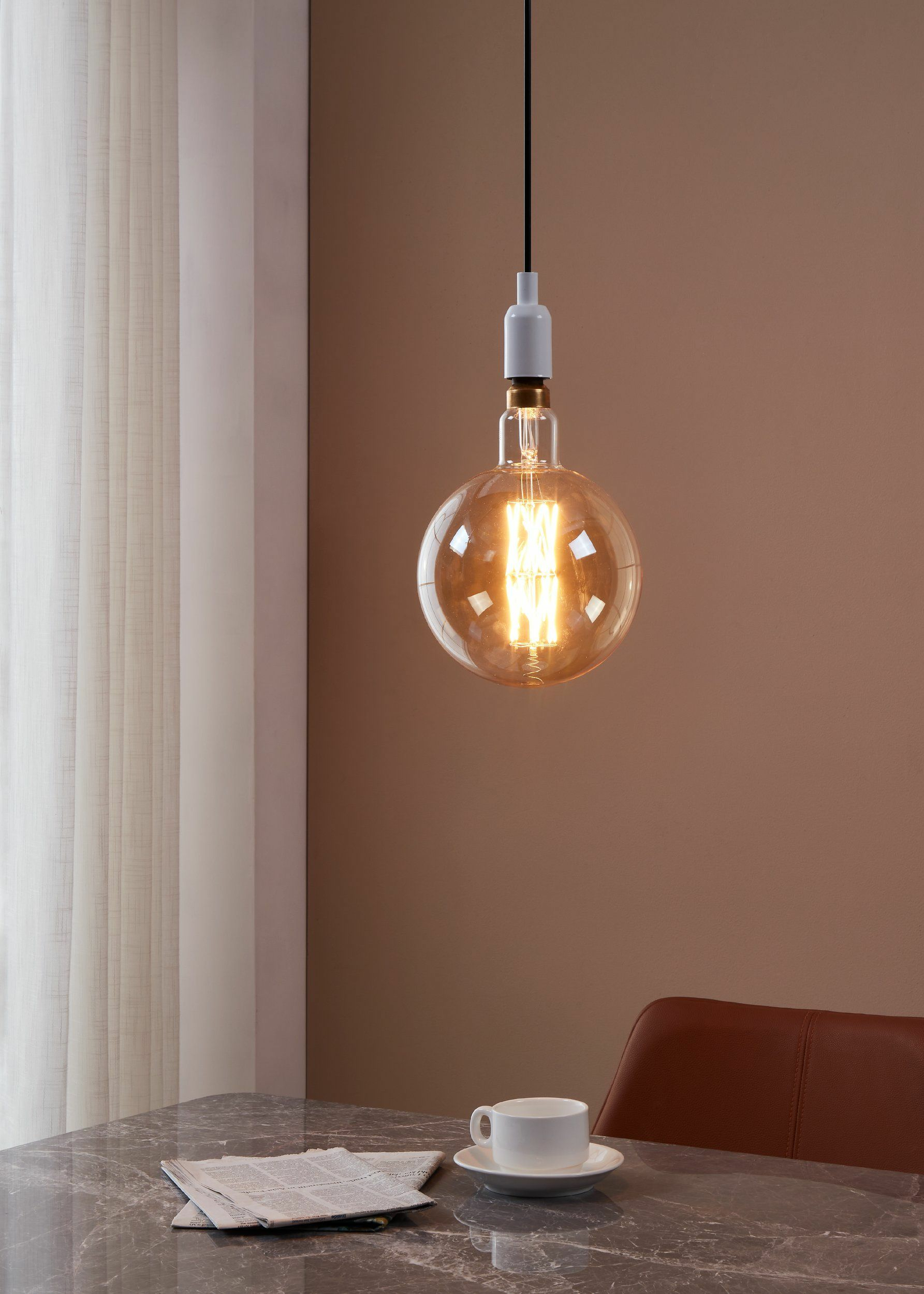 Una lampadina appesa al soffitto. C'è un giornale e una tazza sul tavolo.