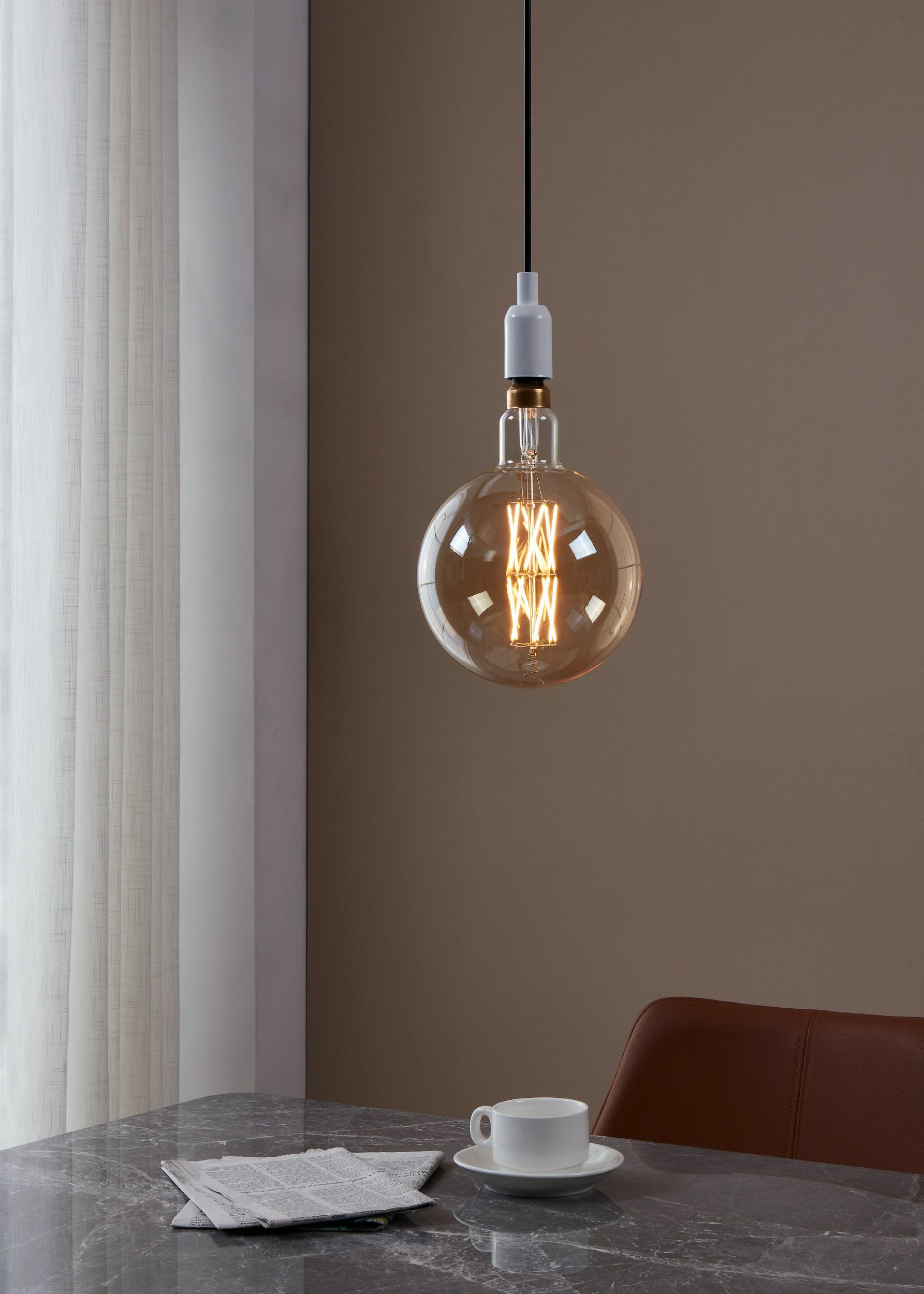 Grande lampadina trasparente appesa sopra un tavolo con giornale e tazza.