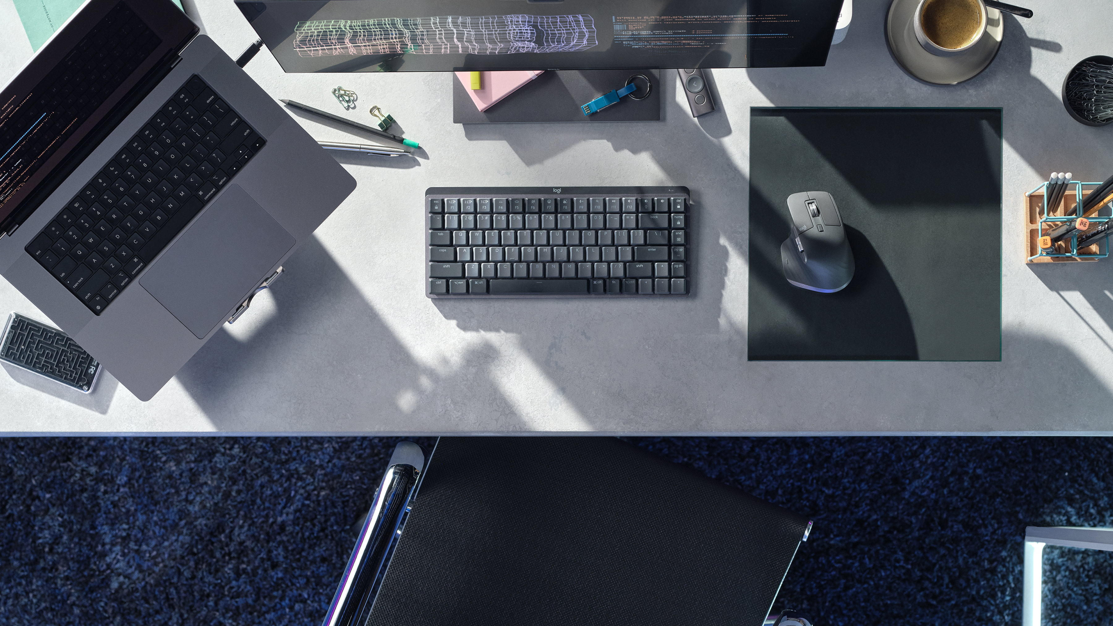 Draufsicht auf einen Schreibtisch mit Laptop, Tastatur, Maus, Becher und anderem Bürobedarf.
