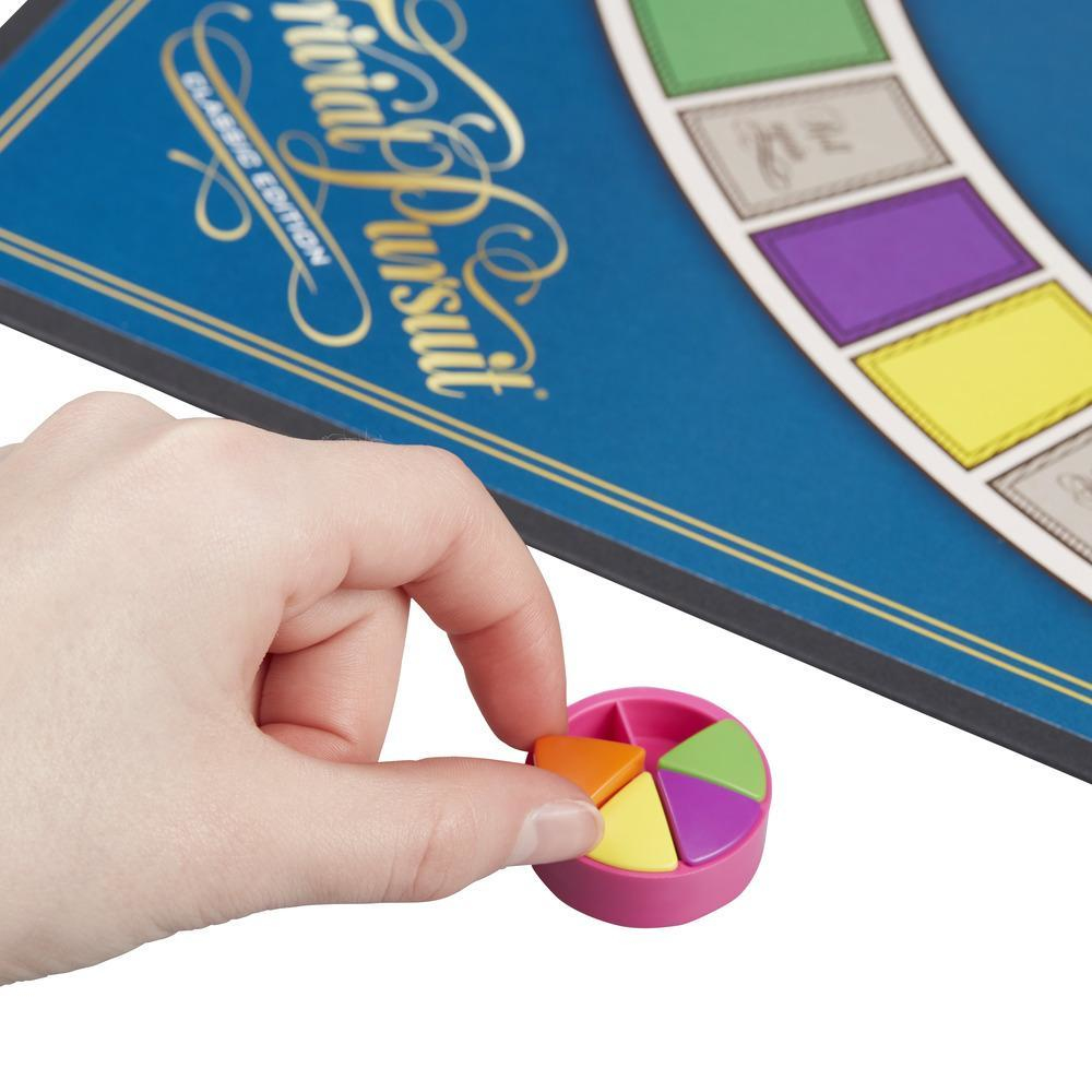 Mano sosteniendo un recipiente rosa con piezas de juego de colores. El juego de mesa es visible.