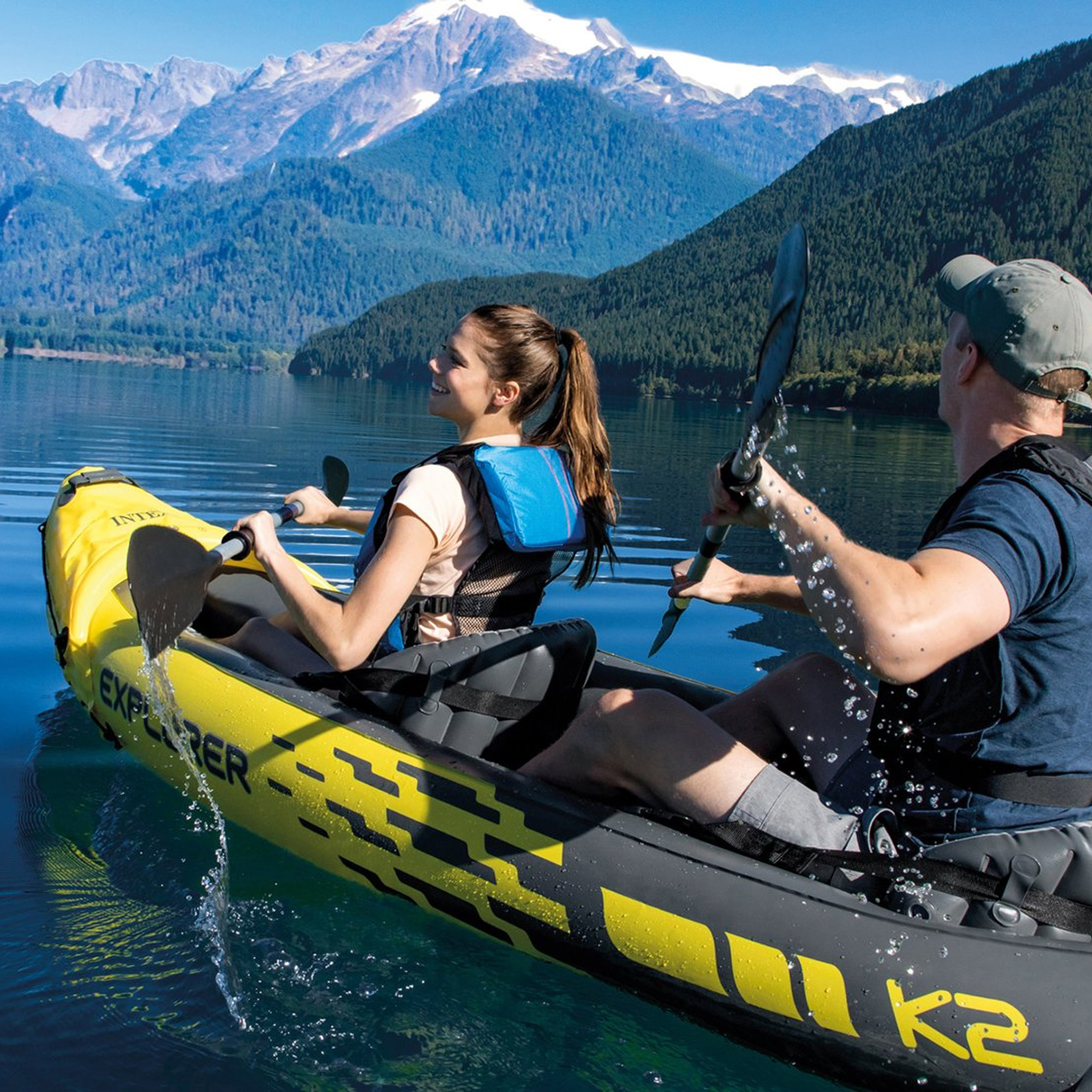 Una coppia in kayak giallo pagaia su un lago, con montagne sullo sfondo e cielo soleggiato.