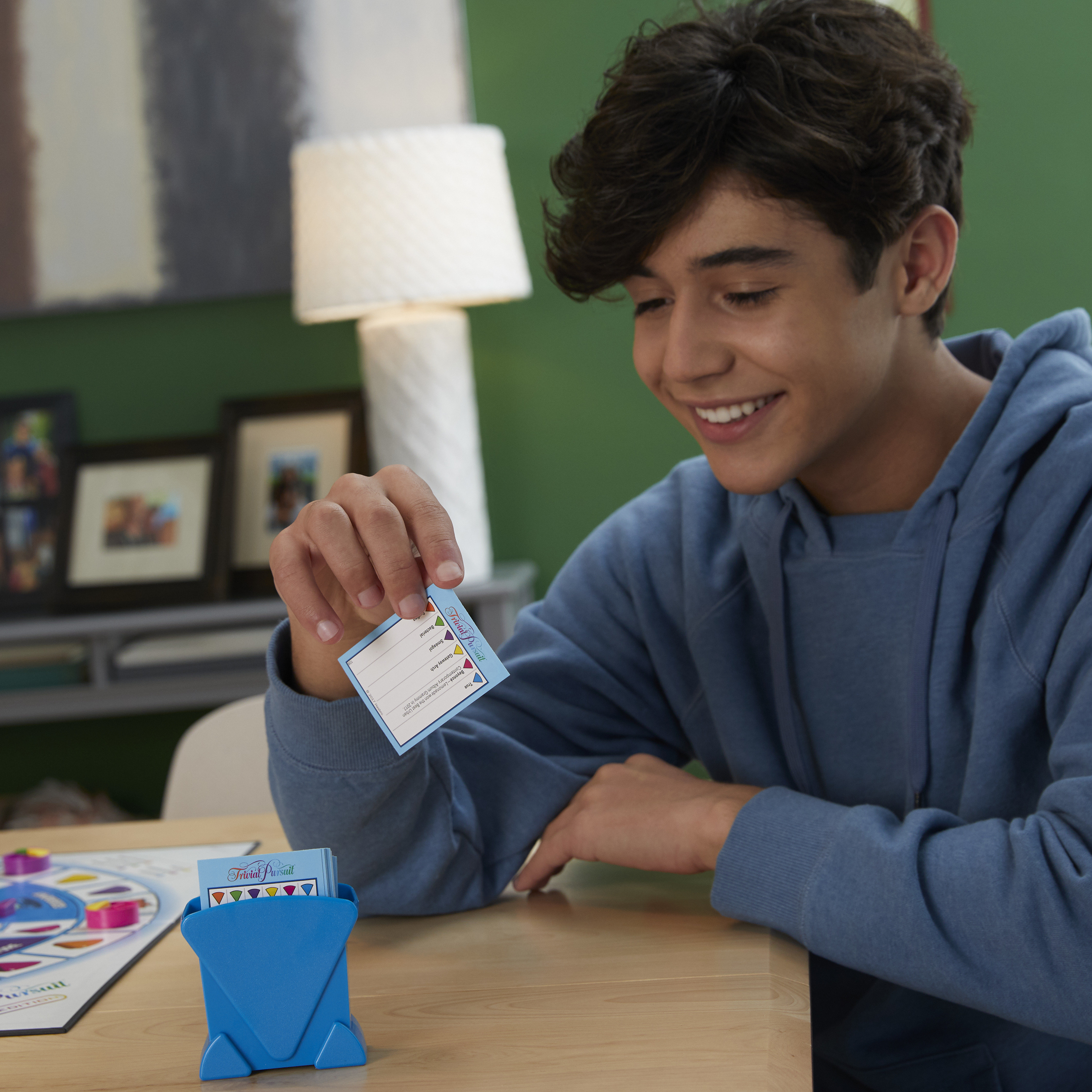 Un adolescent sourit en tenant une carte d'un jeu de société et un porte-cartes.