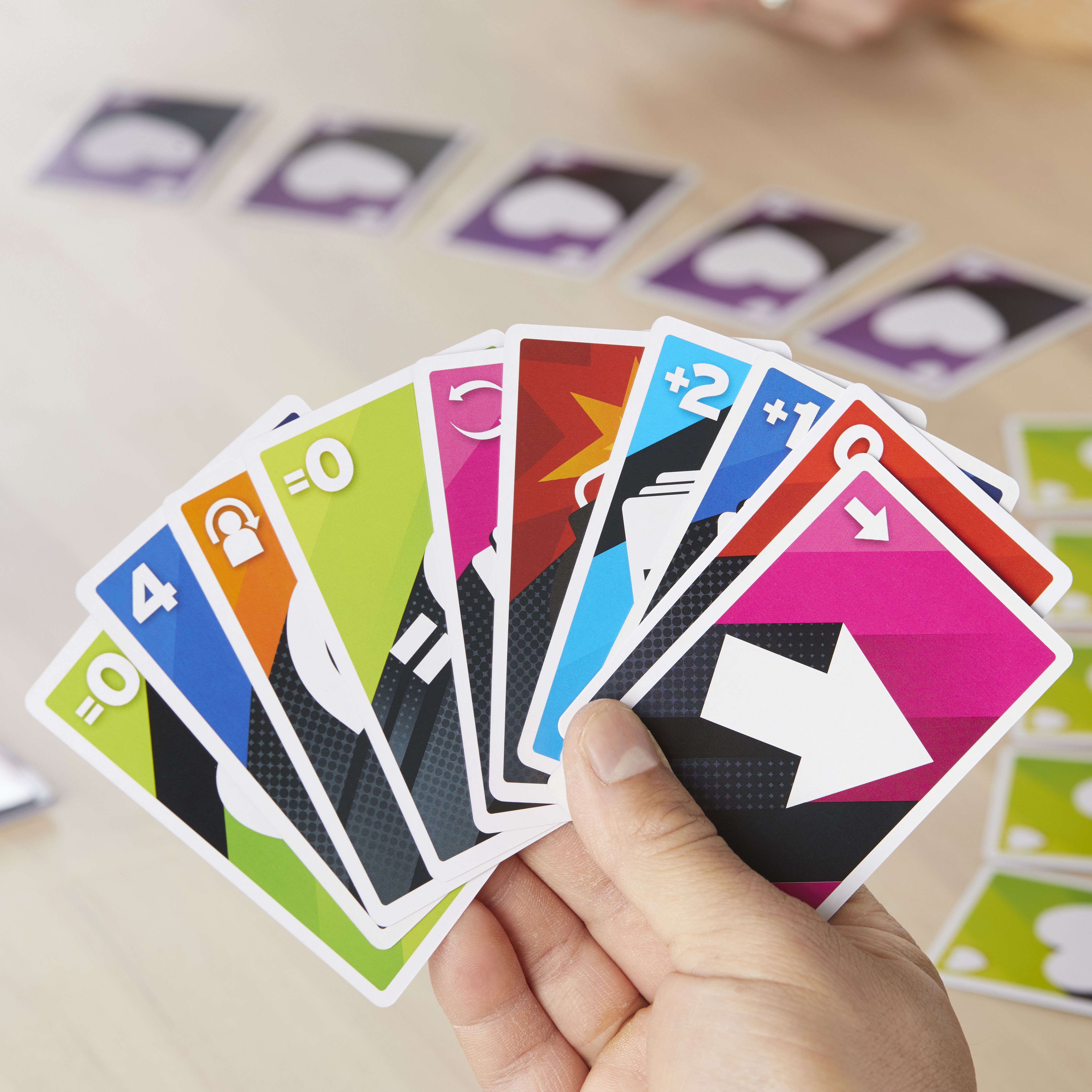 Eine Hand, die Karten eines farbenfrohen Spiels hält. Verschiedene Farben und Symbole sind sichtbar.