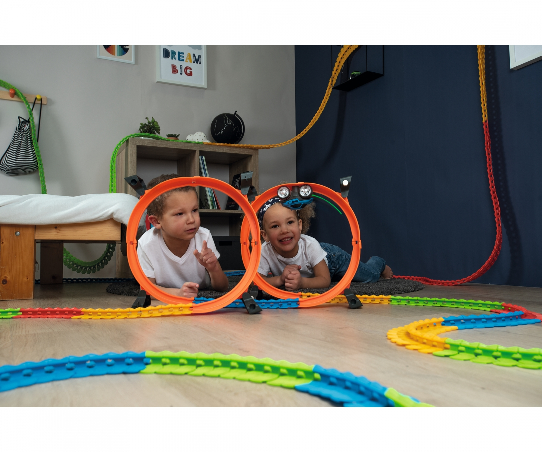 Dwoje dzieci bawiących się torem samochodowym. Pomarańczowe pętle. Ciemne tło.
