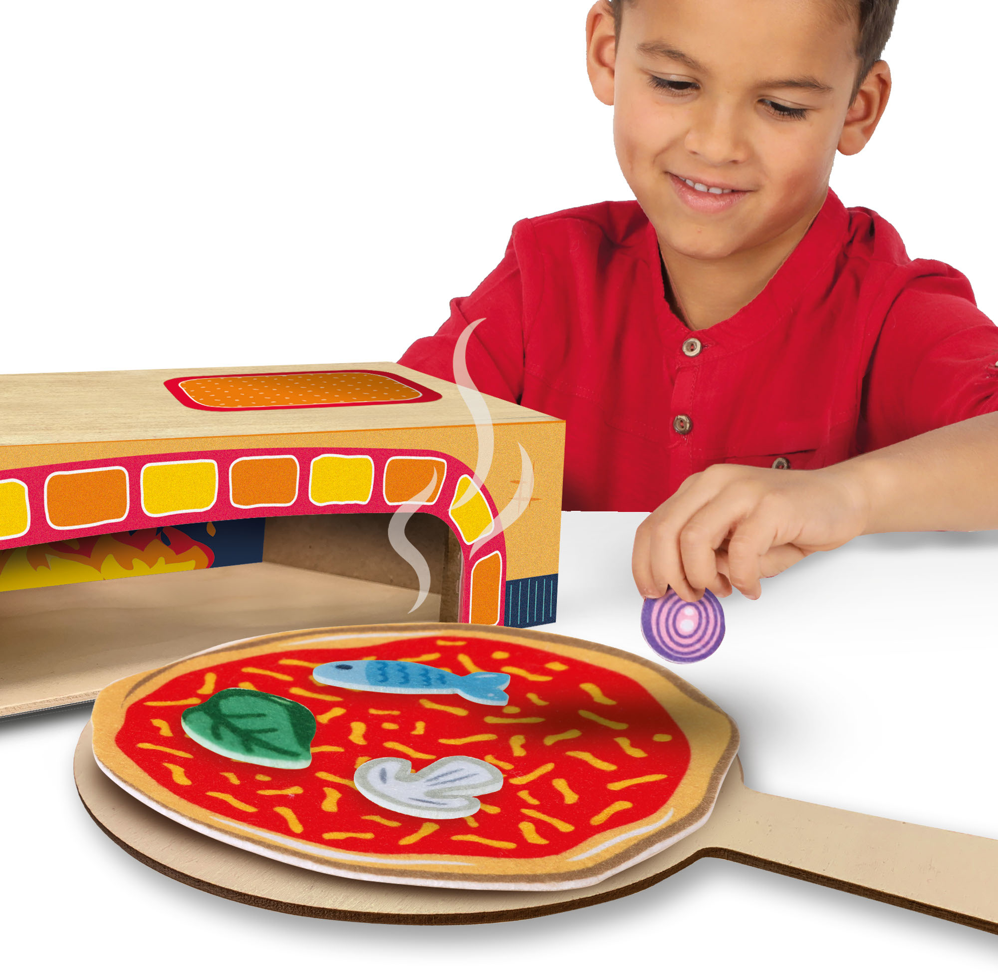 Junge fügt eine lila Zwiebel zu einer Spielzeugpizza auf einem hölzernen Pizzaschieber hinzu, lächelnd.