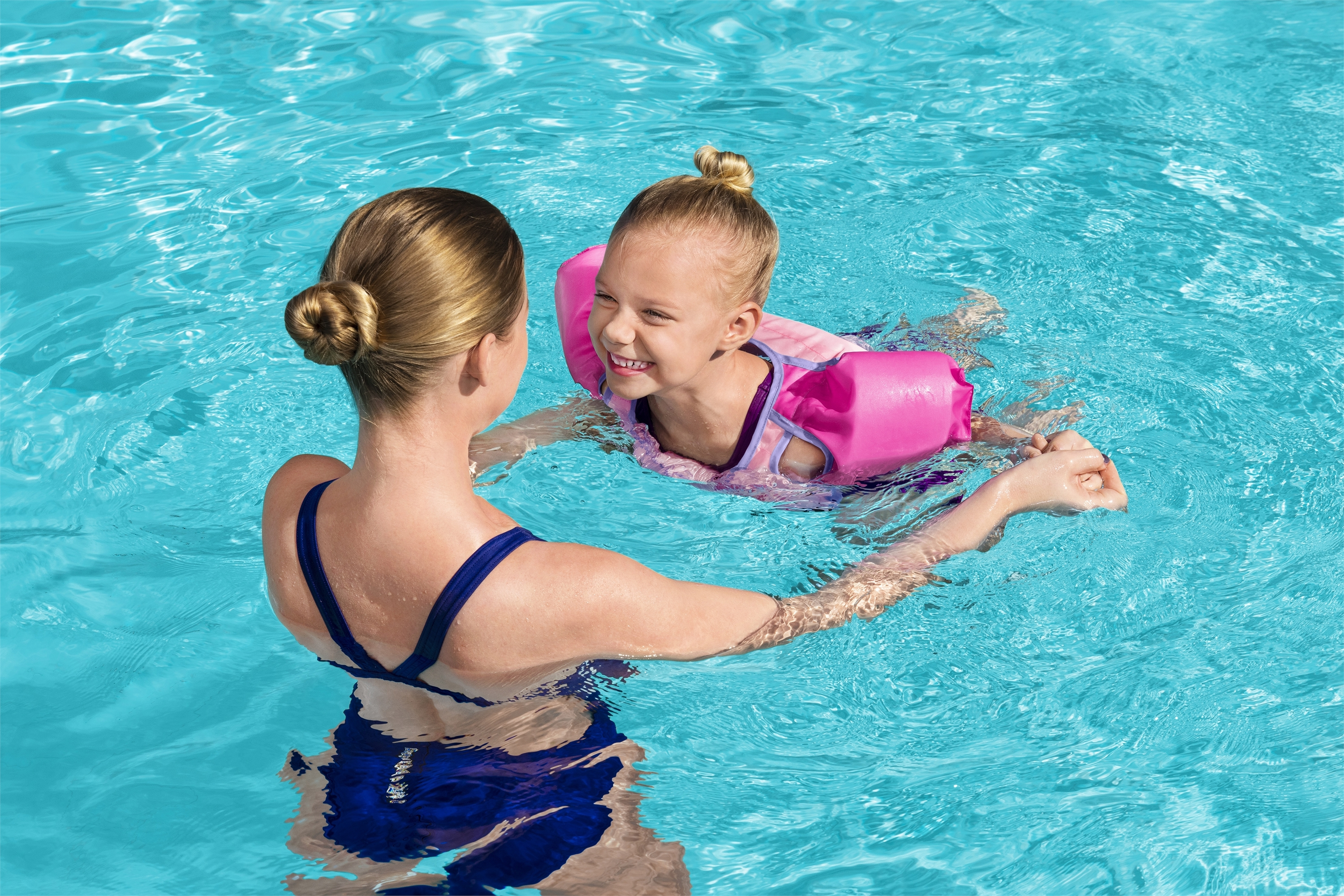 Kobieta i dziecko w basenie. Kobieta w niebieskim stroju kąpielowym, dziecko w różowych rękawkach, uśmiech w basenie.