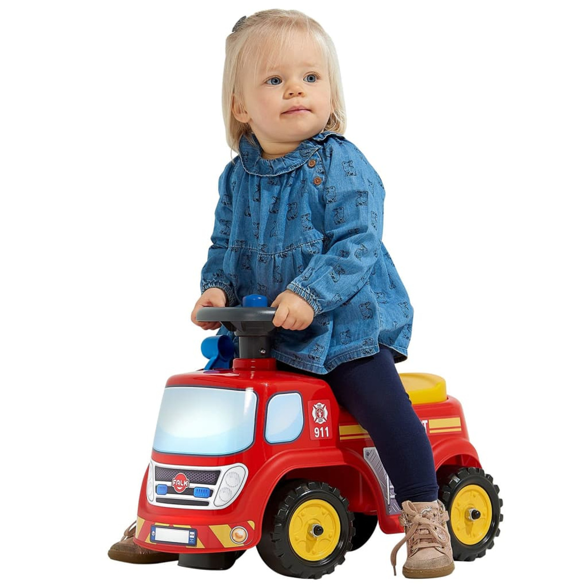 Bambina su un camion dei pompieri giocattolo rosso, seduta e che guarda di lato.