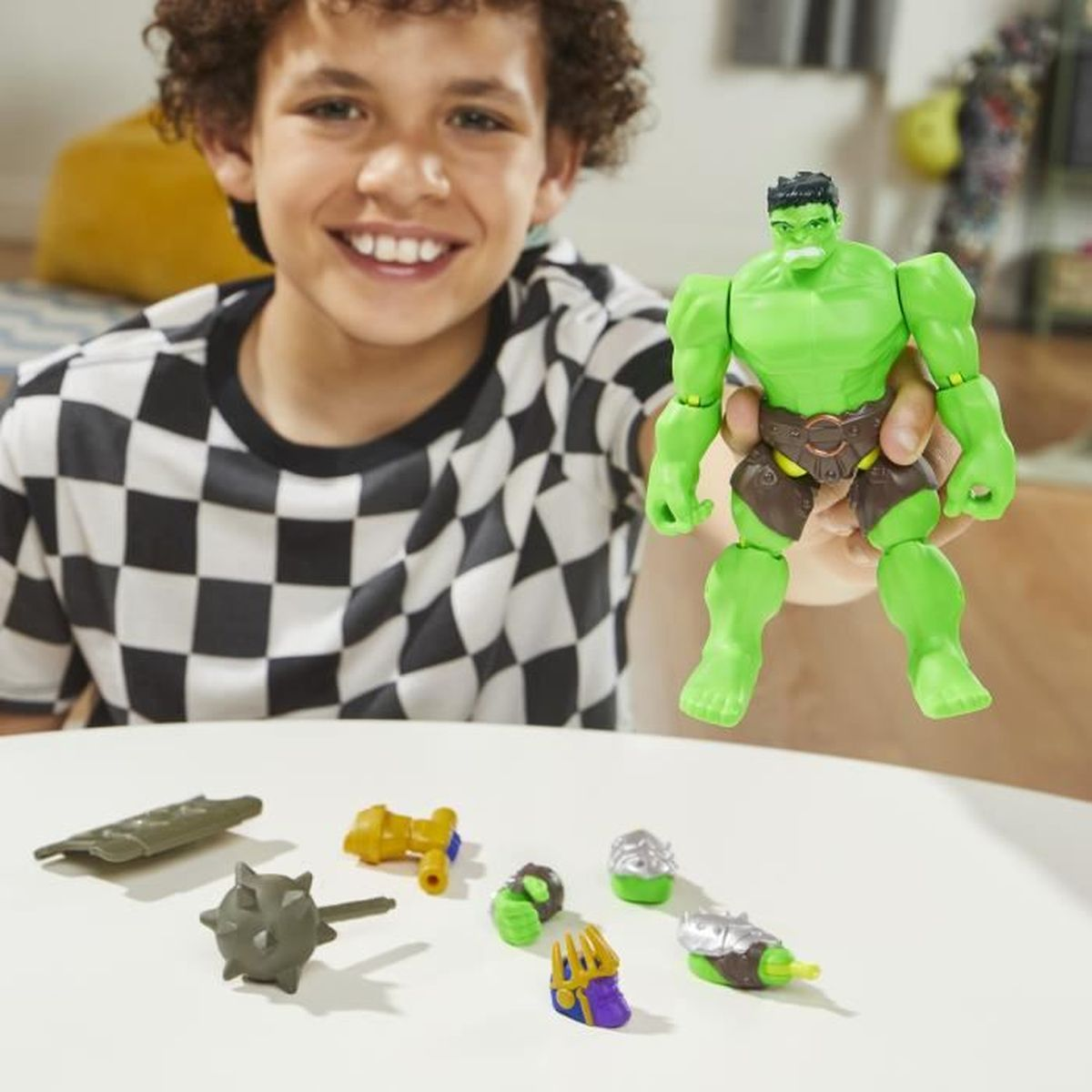 Un niño sonriendo sosteniendo una figura de acción de Hulk. Los accesorios están sobre la mesa. El fondo es una mesa blanca.