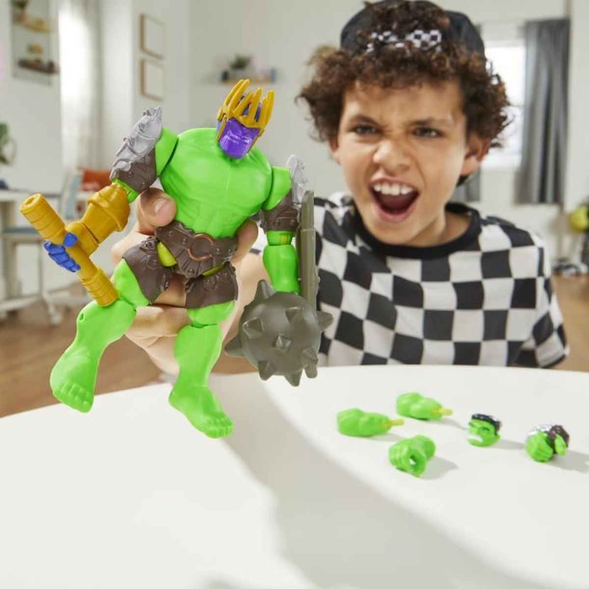 Un niño y una figura de juguete verde. El niño está emocionado. Varias cabezas de juguete en la mesa.