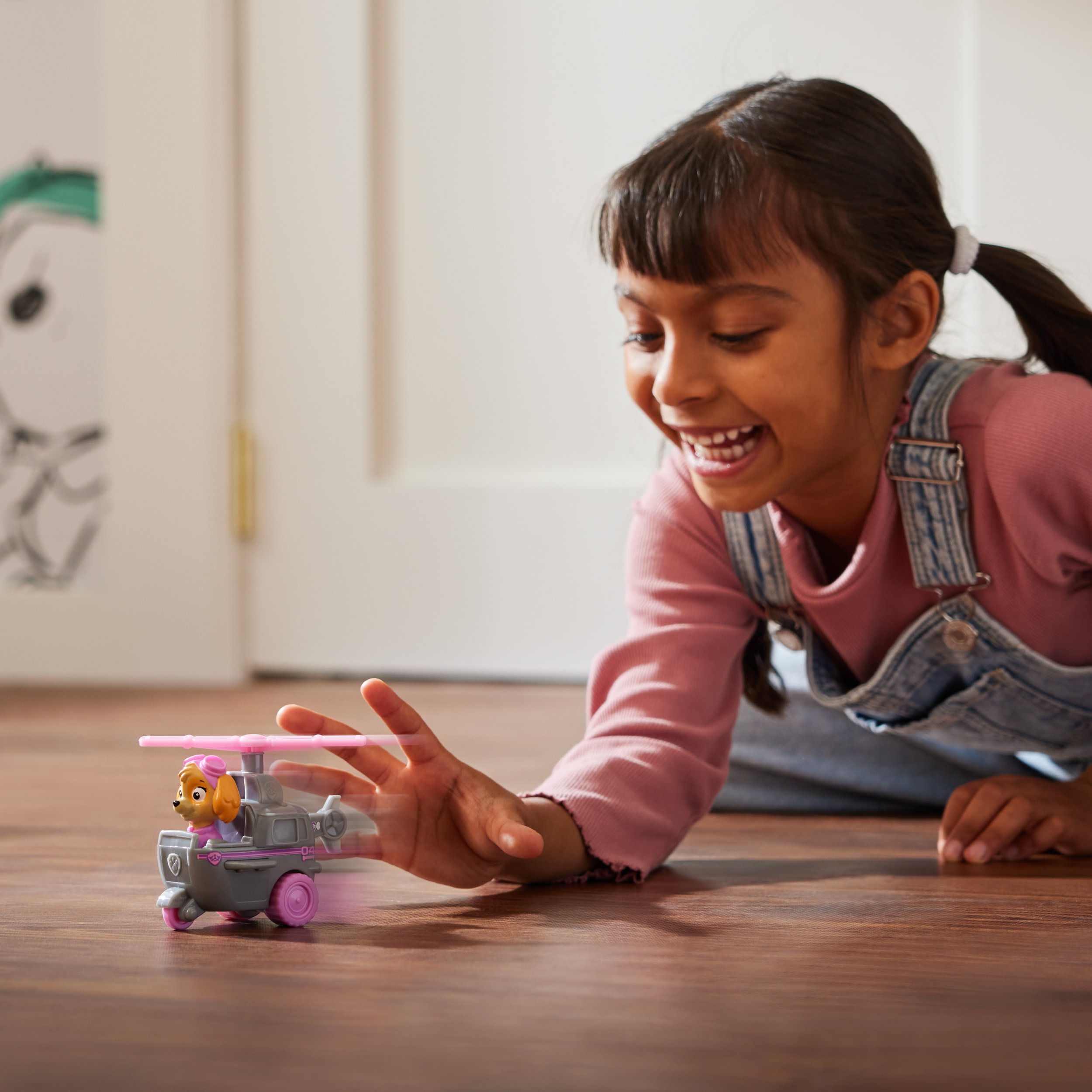 Dziewczynka bawi się zabawką helikopterem. Jest różowy i szary, z uśmiechniętą postacią z kreskówki.