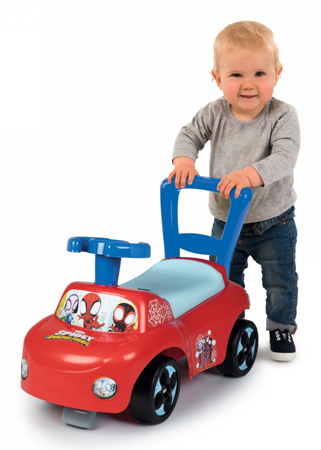 Małe dziecko stoi obok czerwonego samochodu Spider-Mana. Ma niebieski uchwyt i siedzenie, czarne koła i grafikę Spider-Mana.