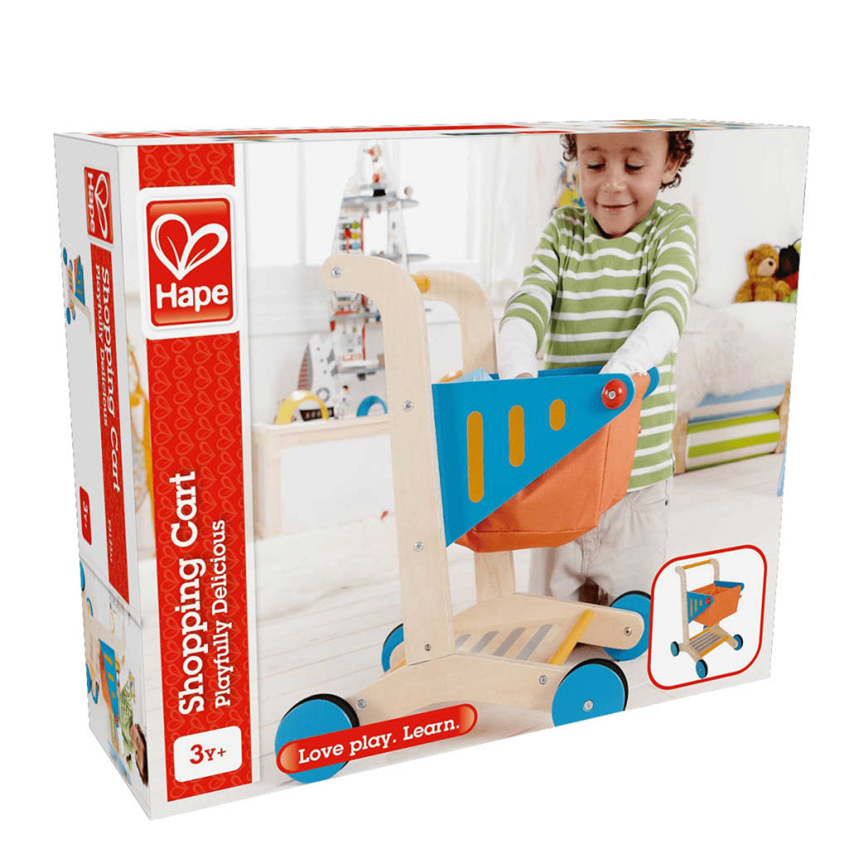 Un niño con una camiseta de rayas está de pie cerca de una caja de carrito de compras de juguete. La caja muestra el carrito y el logo Hape.