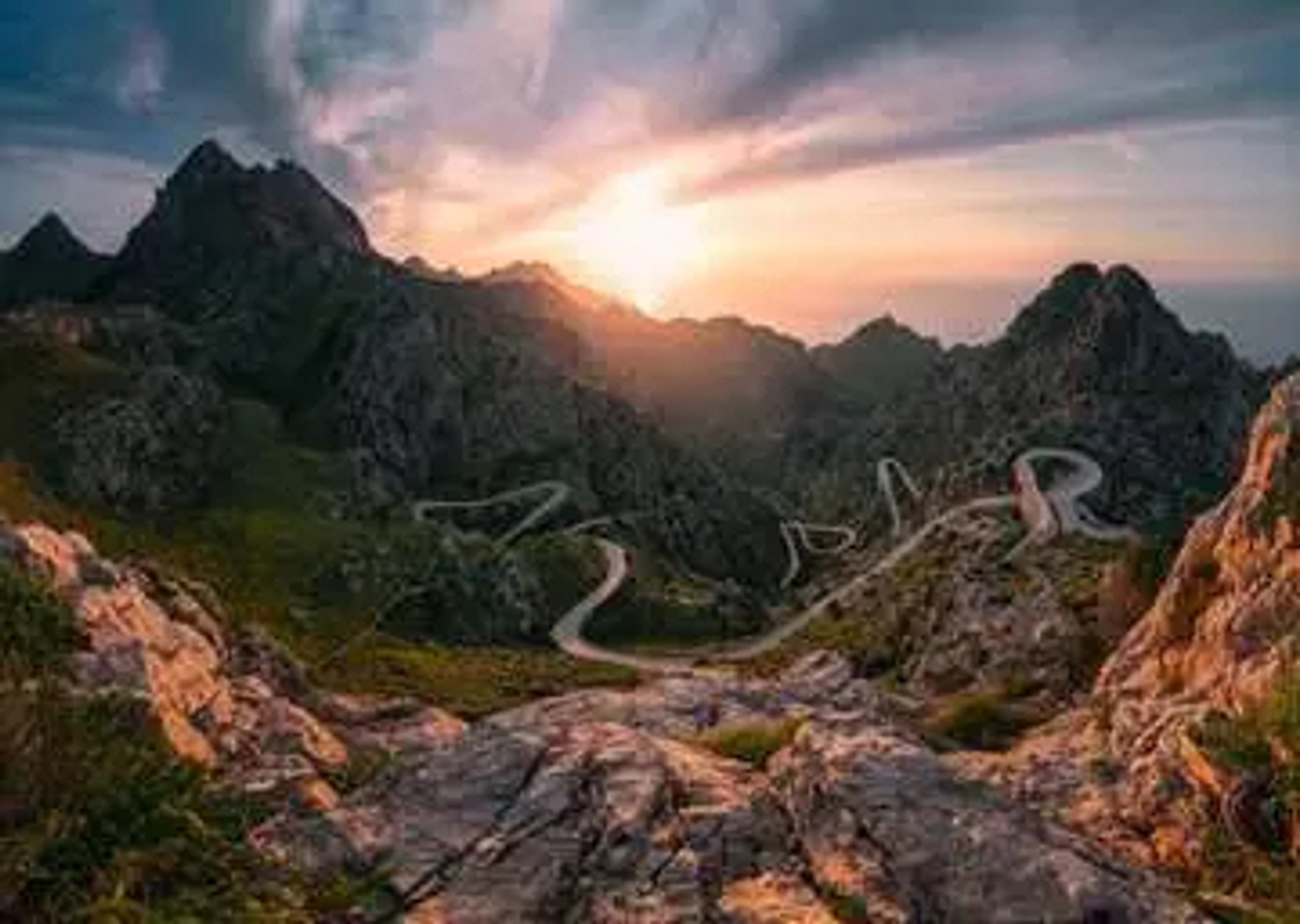 Eine malerische Aussicht auf eine kurvenreiche Straße durch Berge bei Sonnenuntergang.
