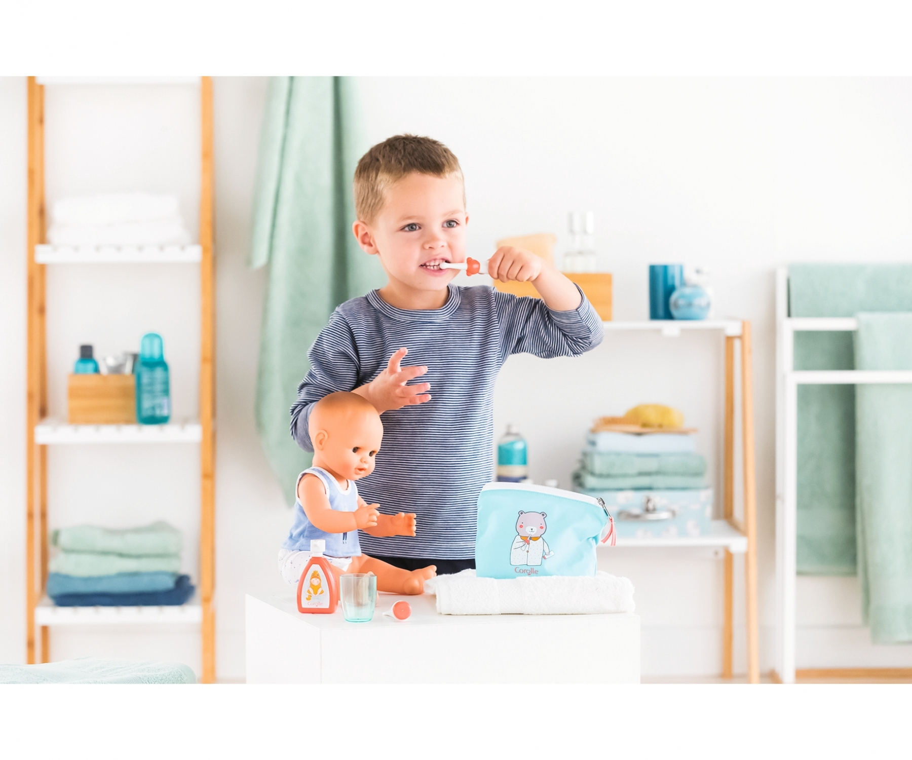 Chłopiec myjący zęby lalce w łazience. Lalka siedzi na białej powierzchni. Akcesoria łazienkowe w tle.