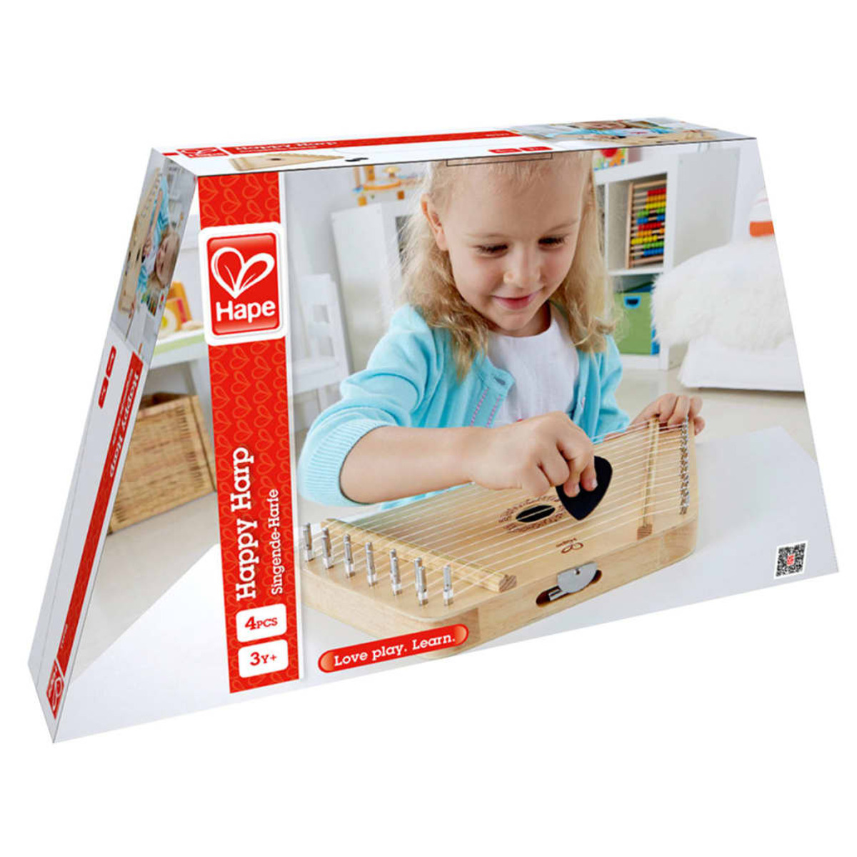 Un niño toca un arpa de juguete de madera. La caja es roja y blanca, y el fondo es una habitación.