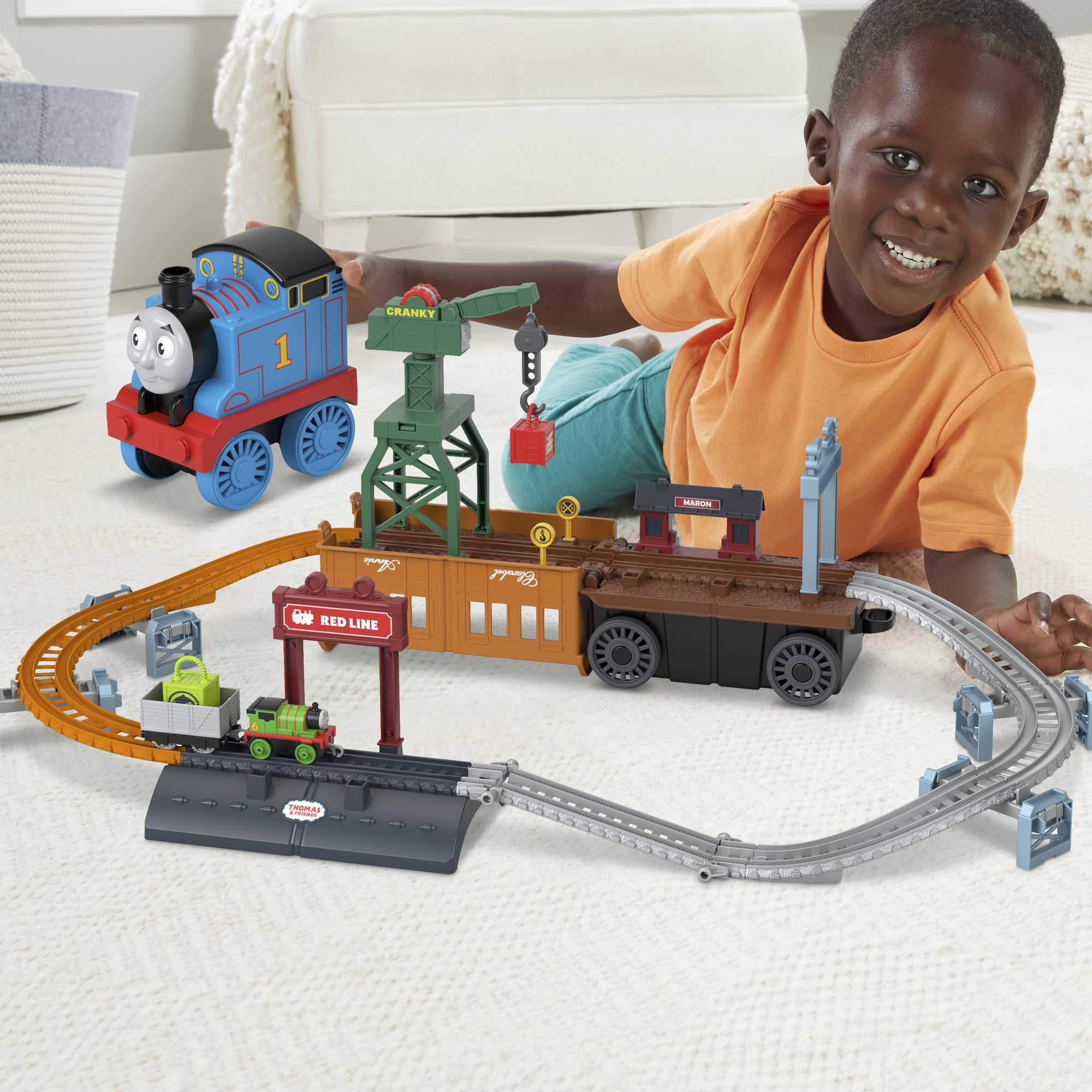 Ein Junge spielt mit einem Spielzeug-Eisenbahn-Set. Blauer Thomas und andere Züge sind sichtbar.