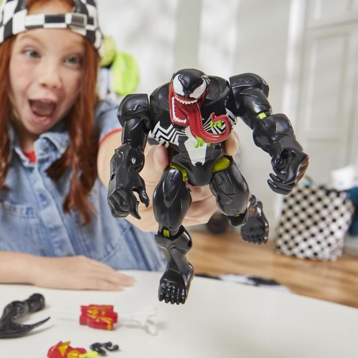 Un niño sosteniendo un juguete de Venom con una gran lengua roja, con otras piezas de juguete sobre una mesa.
