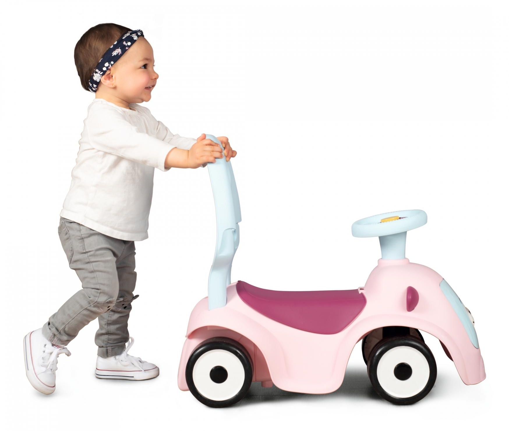 Ein Kleinkind schiebt ein rosa und blaues Spielzeugauto.