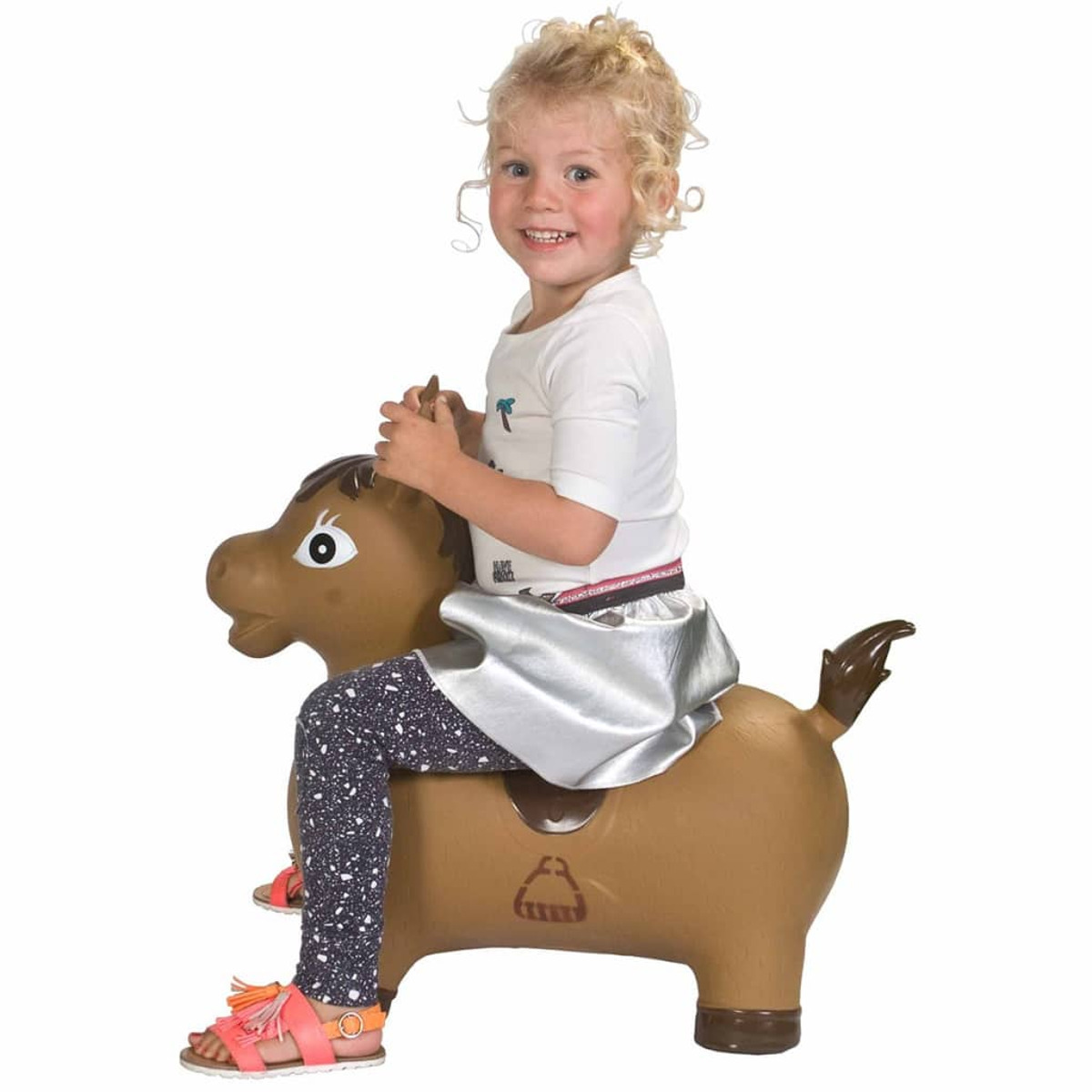 Ragazza che cavalca un giocattolo gonfiabile a forma di cavallo marrone. Sta sorridendo. Top bianco, gonna argentata e sandali rosa.