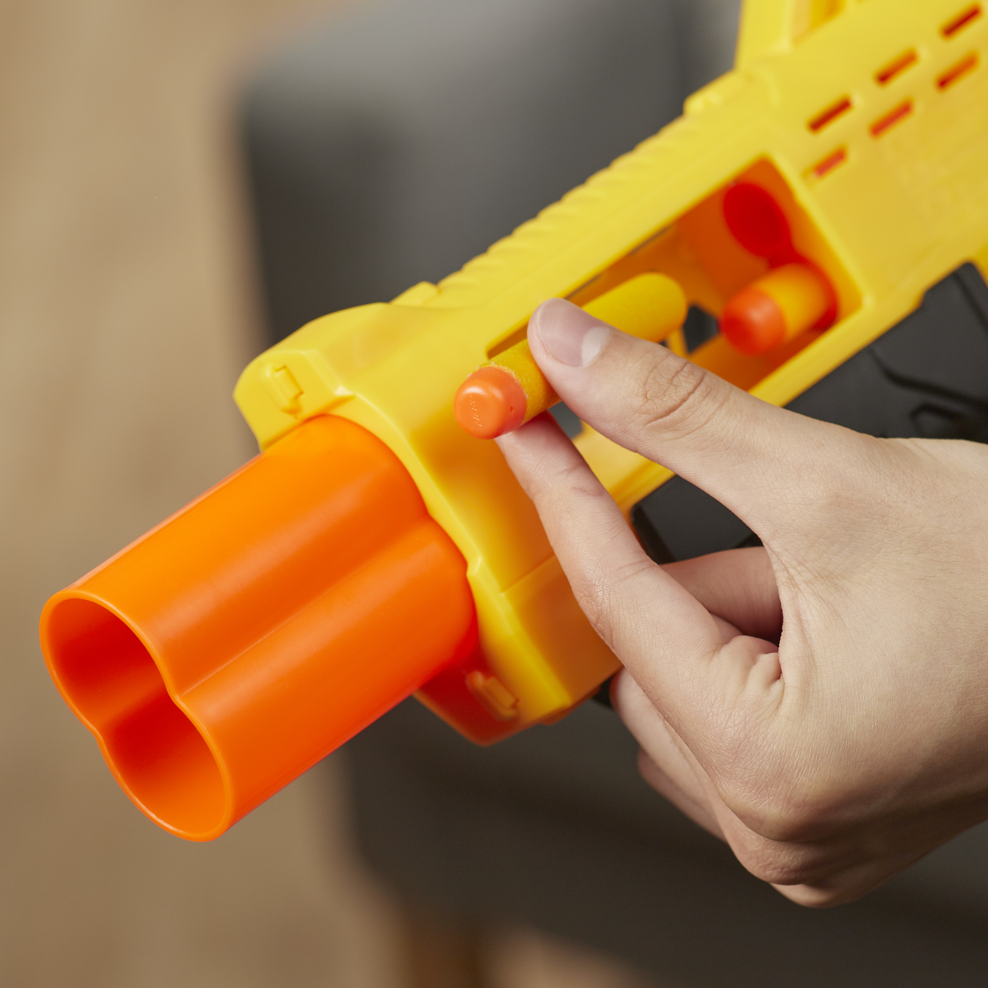 Una mano sosteniendo una pistola Nerf amarilla. Se ven cañones naranjas y dardos naranjas.