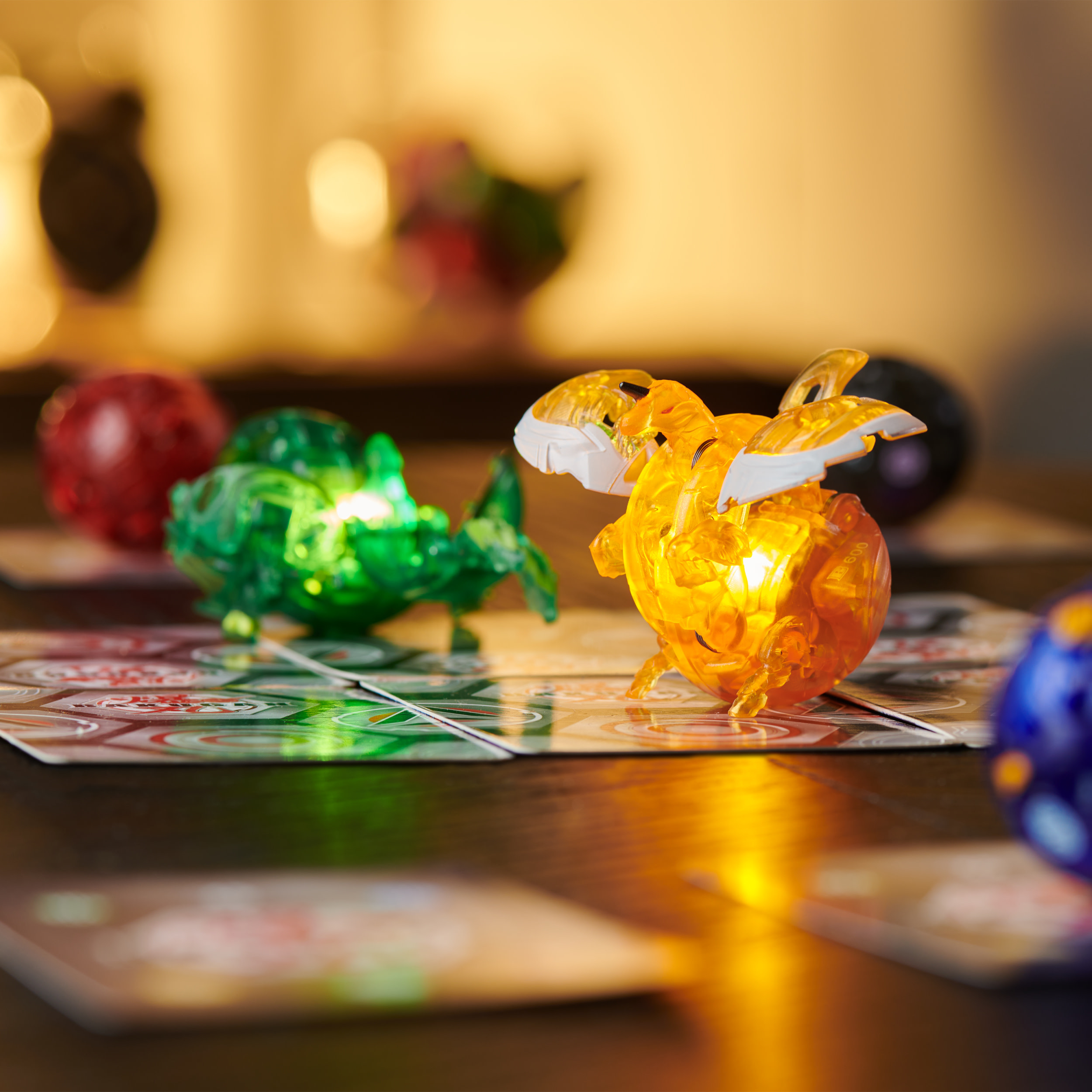 Figuras de Bakugan sobre una mesa. Bolas naranjas y verdes brillantes con cartas.