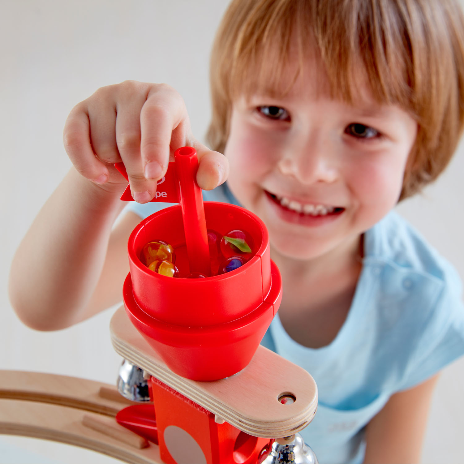 Młody chłopiec trzymający czerwoną zabawkę z płynami i kolorowymi kulkami. Chłopiec się uśmiecha.