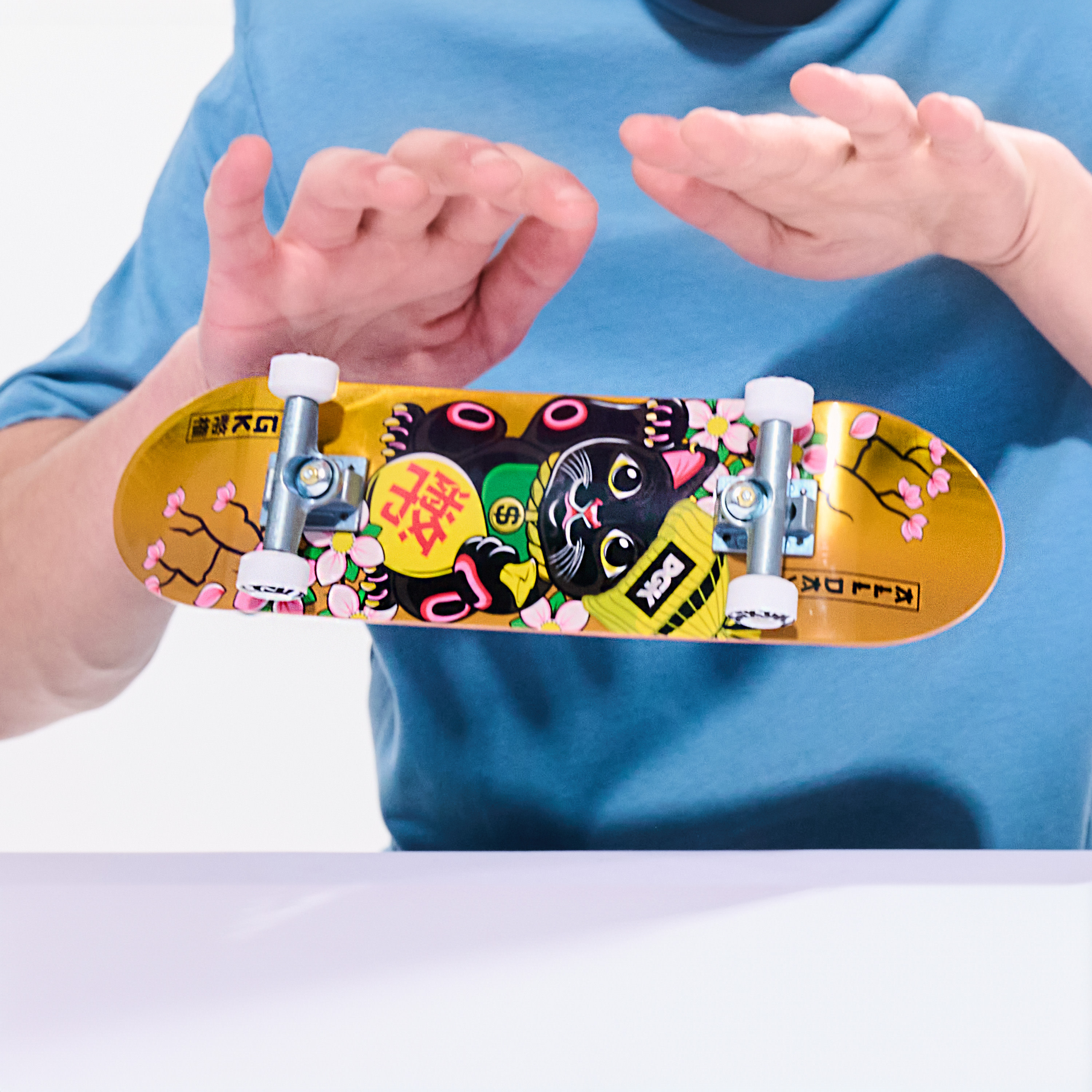 Osoba trzyma złotą deskorolkę fingerboard z czarnym kotem.