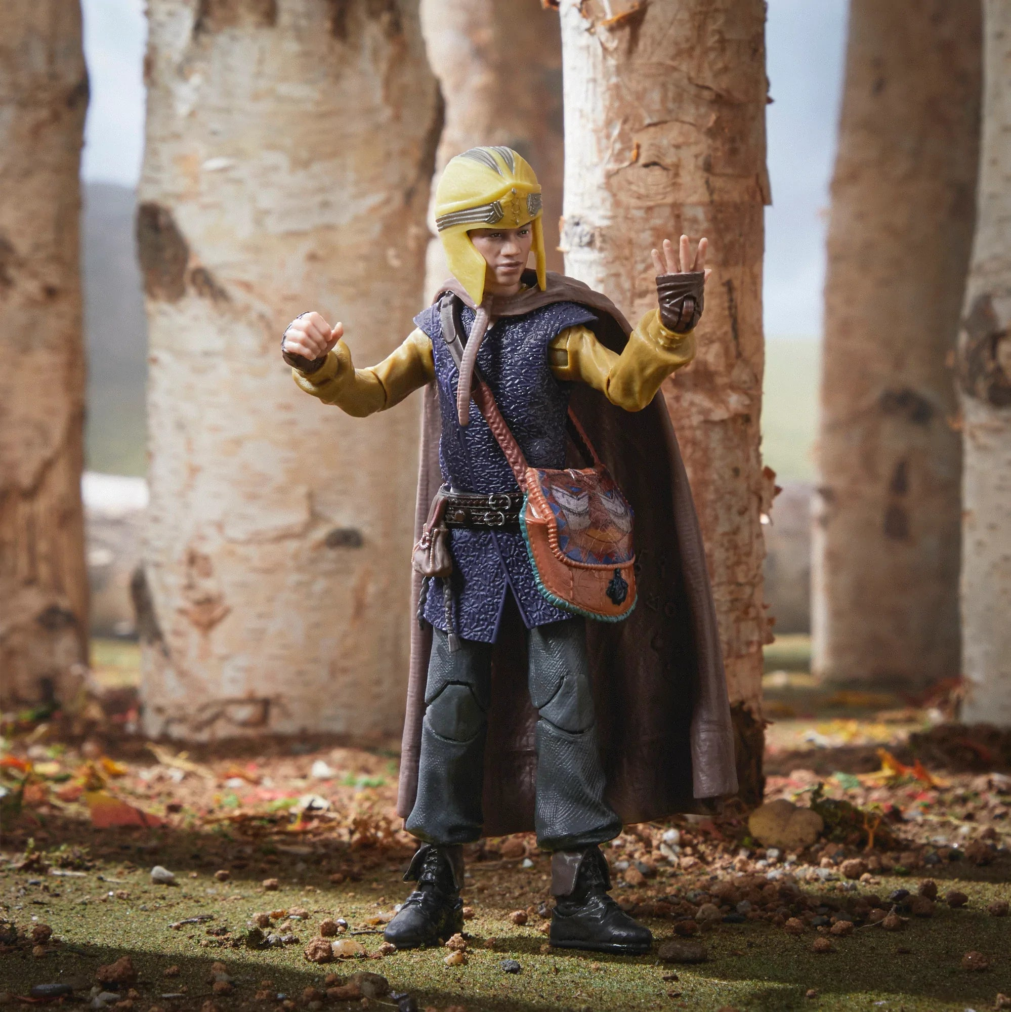 Una figura giocattolo di una persona in abito in stile medievale in piedi in un ambiente forestale.