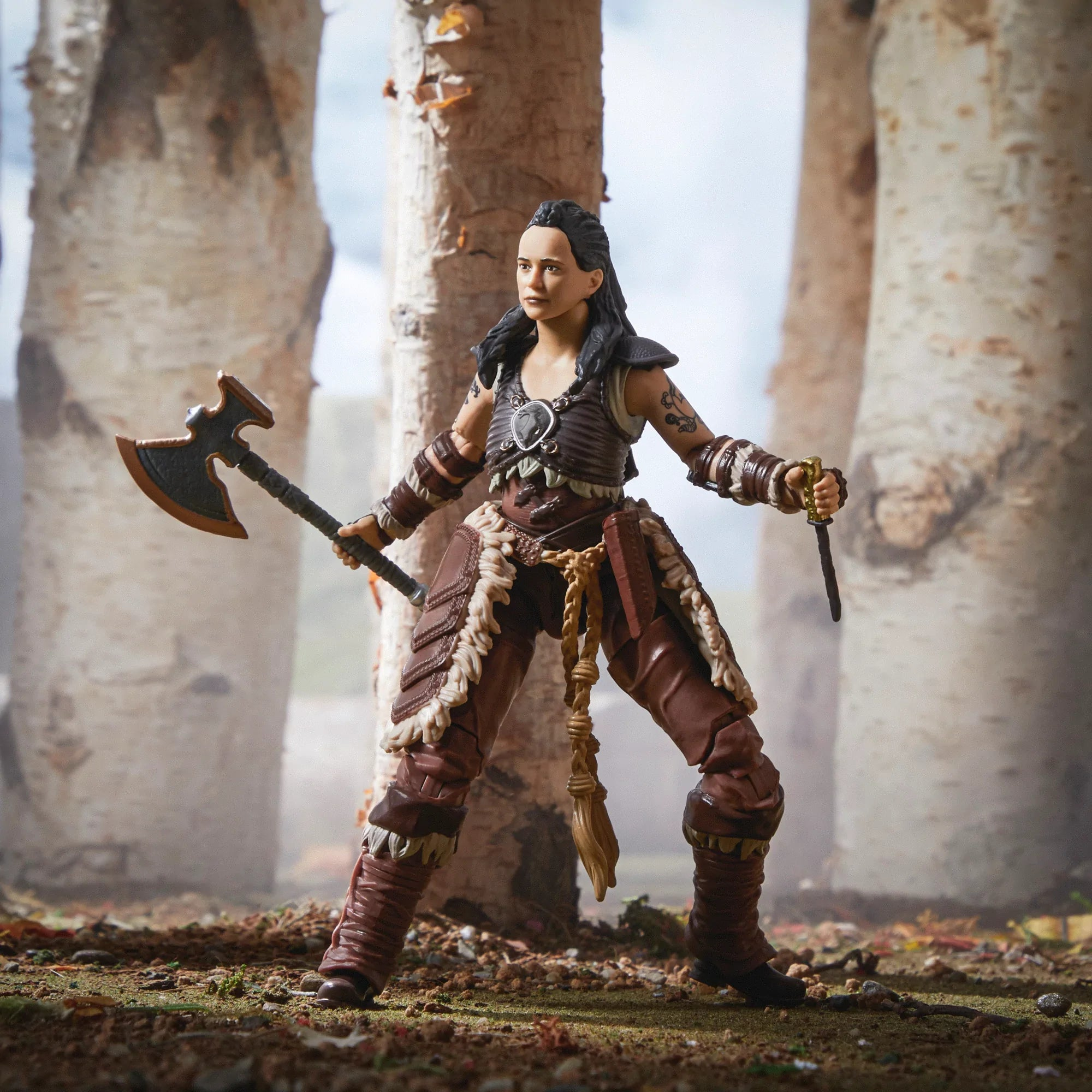 Una action figure femminile che tiene un'ascia e un coltello. Indossa un'armatura marrone ed è in piedi.