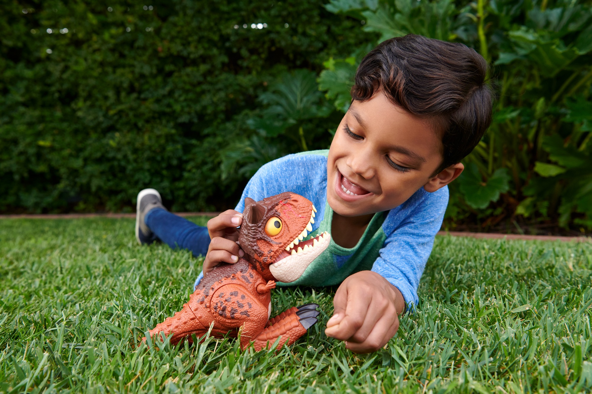 Chłopiec trzymający zabawkę dinozaura na trawniku.