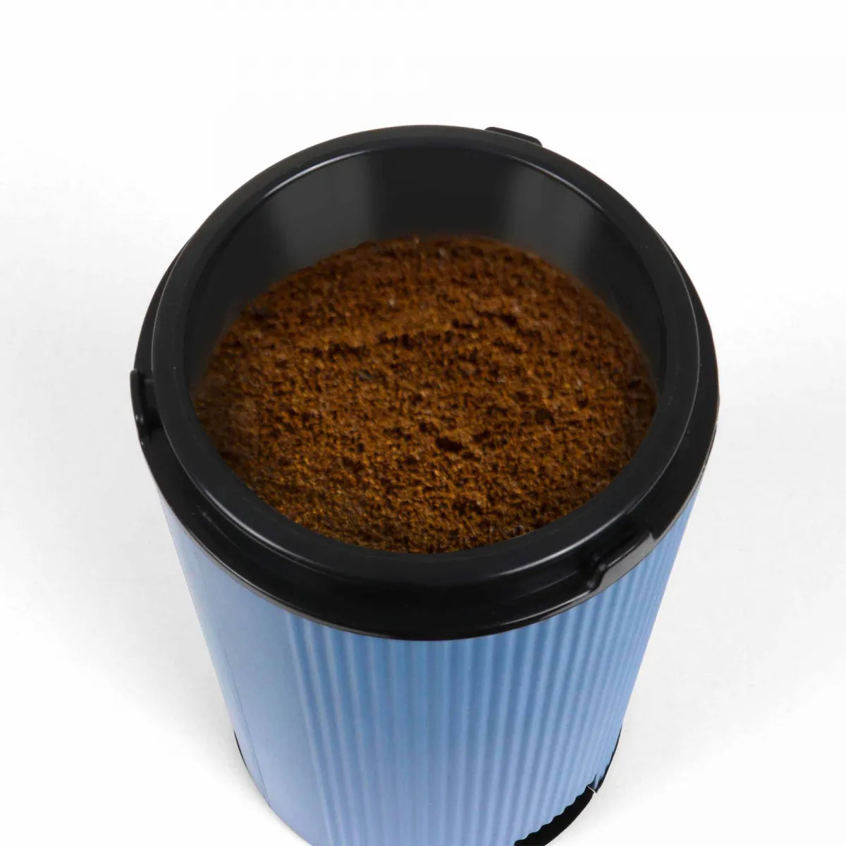 Niebiesko-czarny pojemnik wypełniony brązowymi fusami kawy, na białym tle.