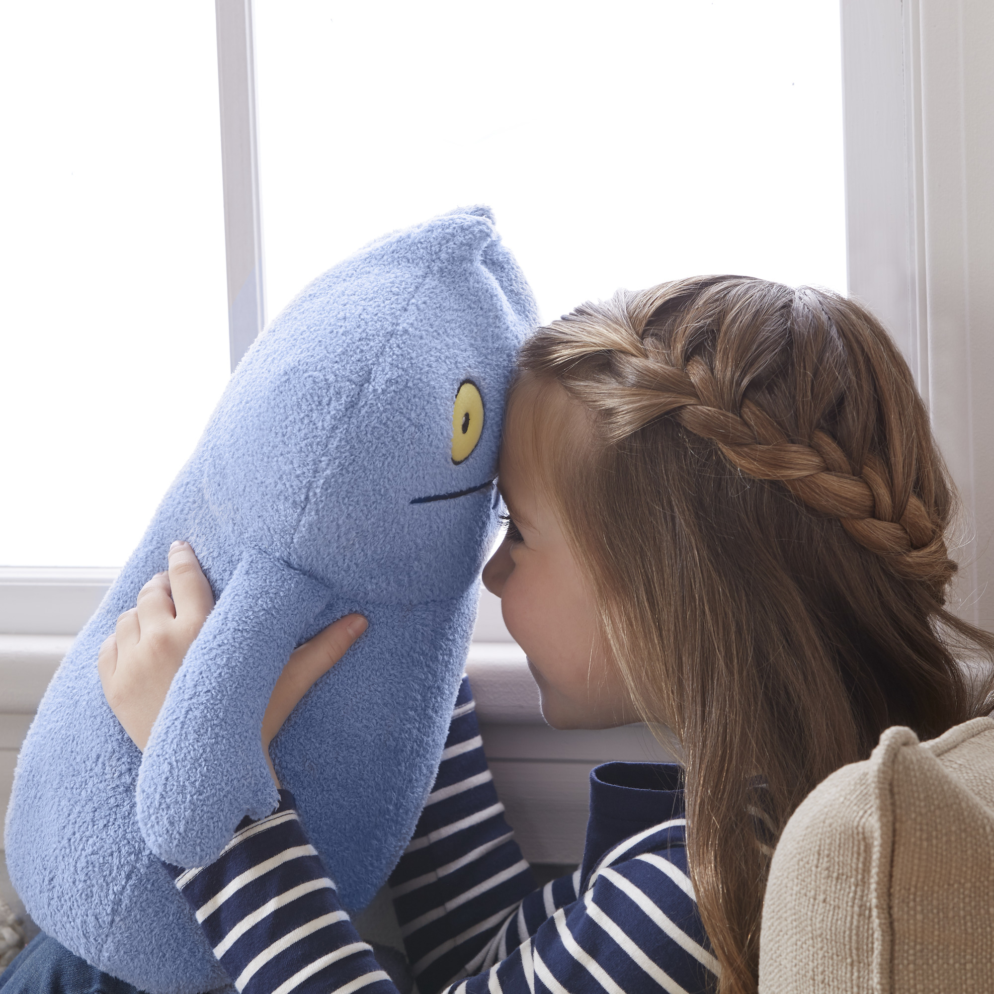 Ein Mädchen umarmt ein blaues Plüschtier. Das Mädchen hat lange braune Haare und trägt ein gestreiftes Hemd. Das Spielzeug ist blau.