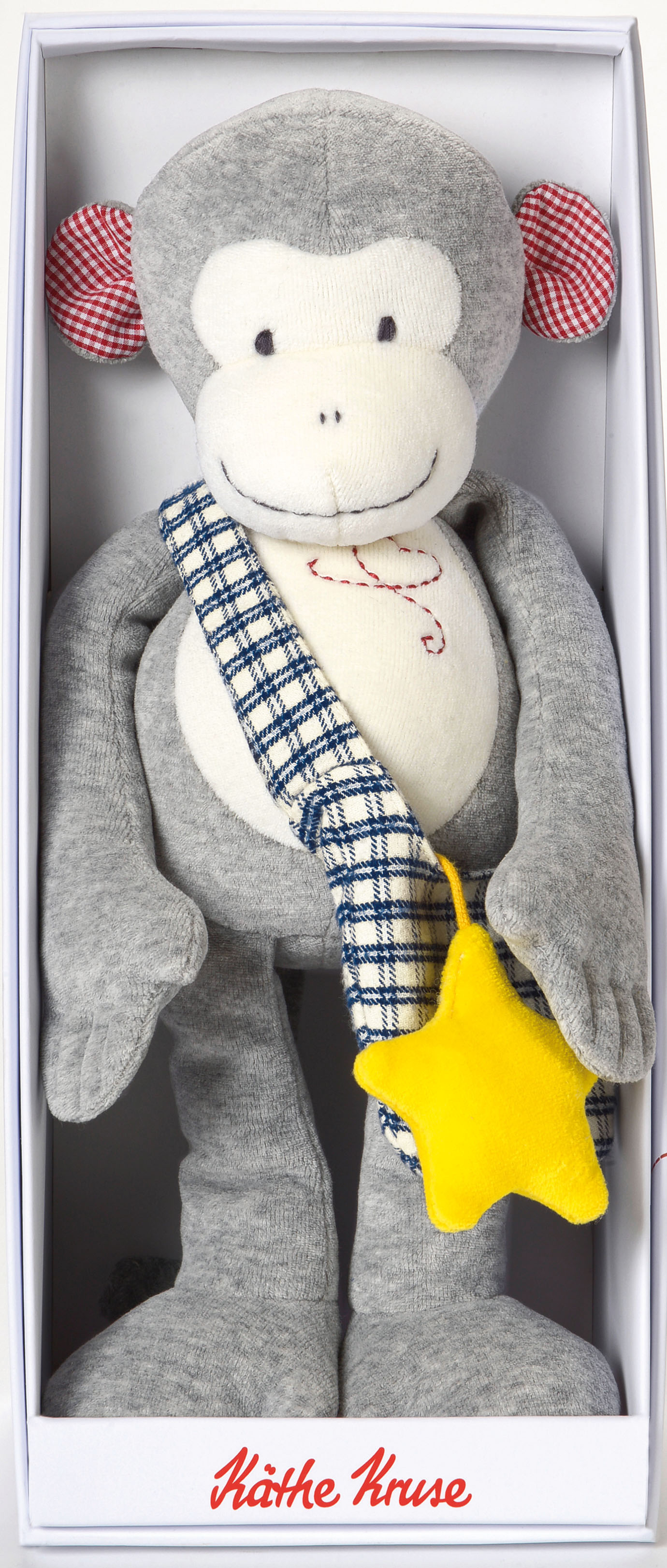 Un juguete de peluche de mono en una caja. El mono tiene pelaje gris, cara blanca y una estrella en el pecho.
