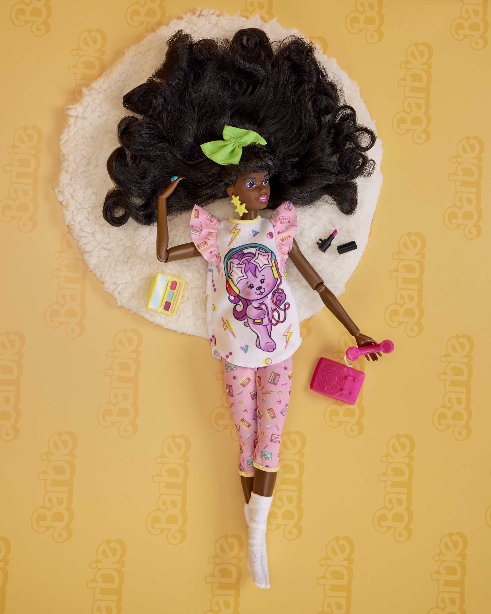 Schwarze Puppe auf flauschigem Teppich, rosa Pyjama, grüner Schleife. Make-up und Telefon.