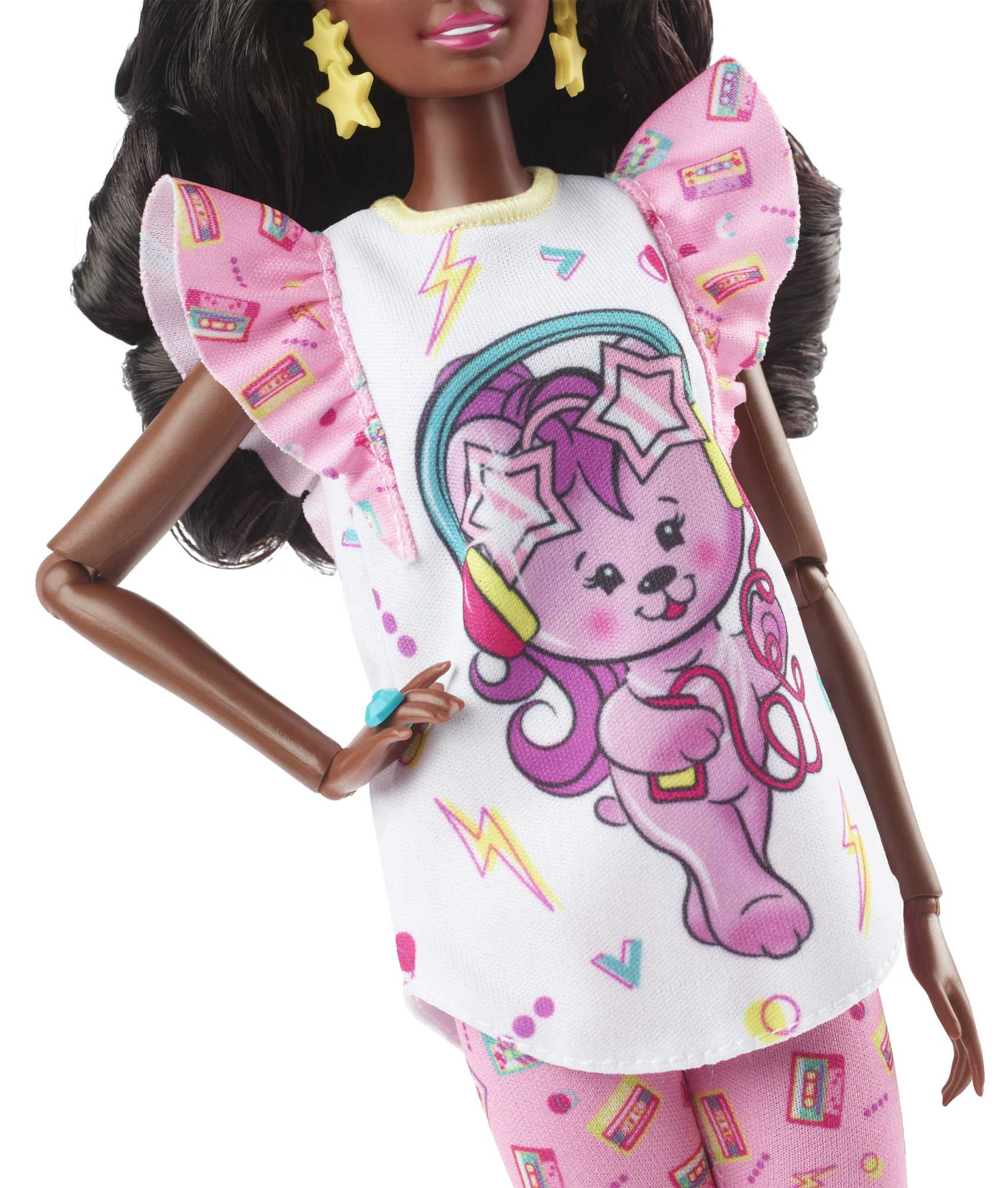 Eine Puppe trägt ein weißes Hemd mit Bärendesign und rosa Hose. Sie hat dunkle Haare.