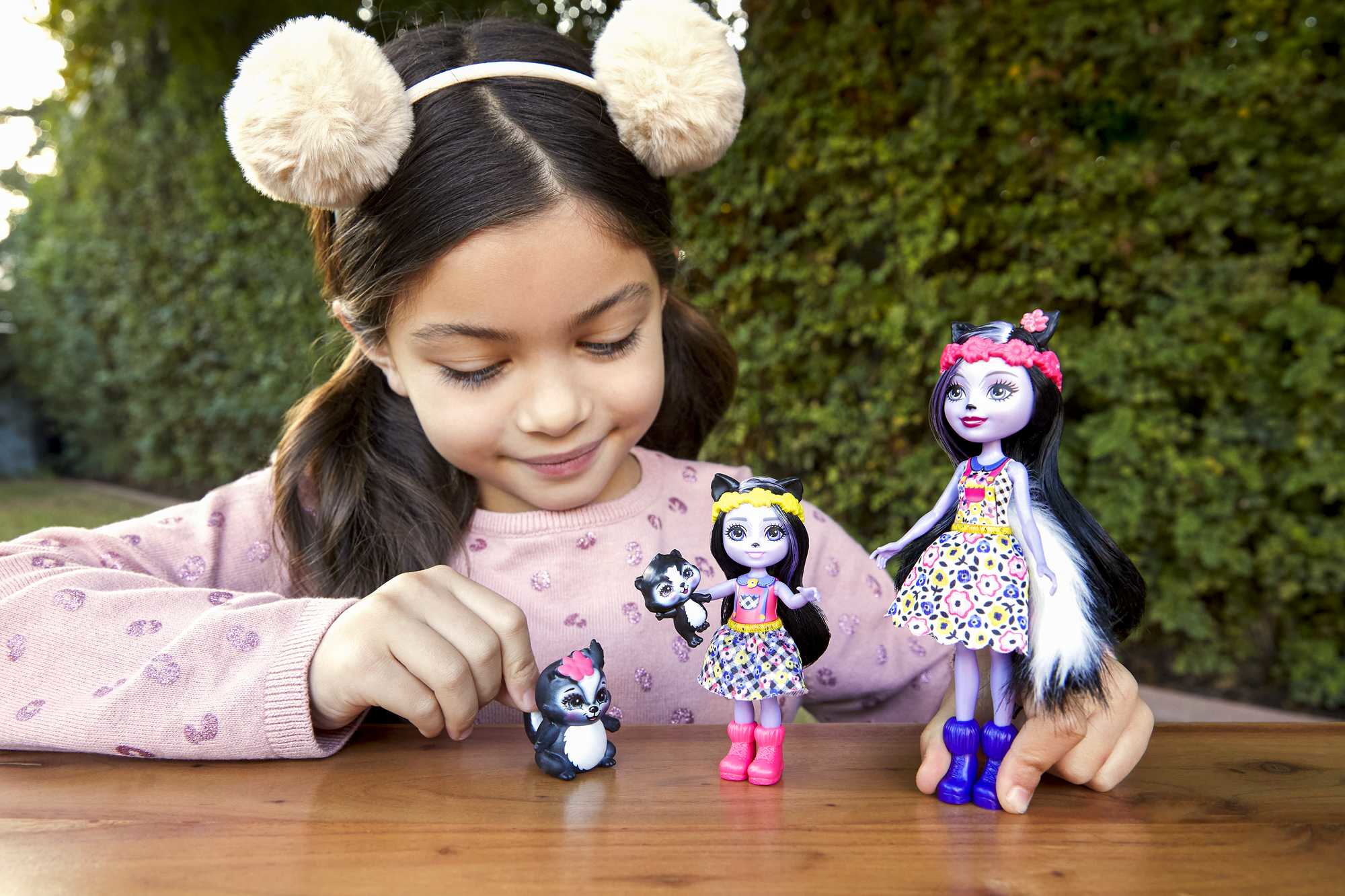 Ein Kind spielt mit Stinktierpuppen. Eine kleine Stinktierfigur und zwei Stinktierpuppen stehen auf einem Tisch. Der Hintergrund ist grün.