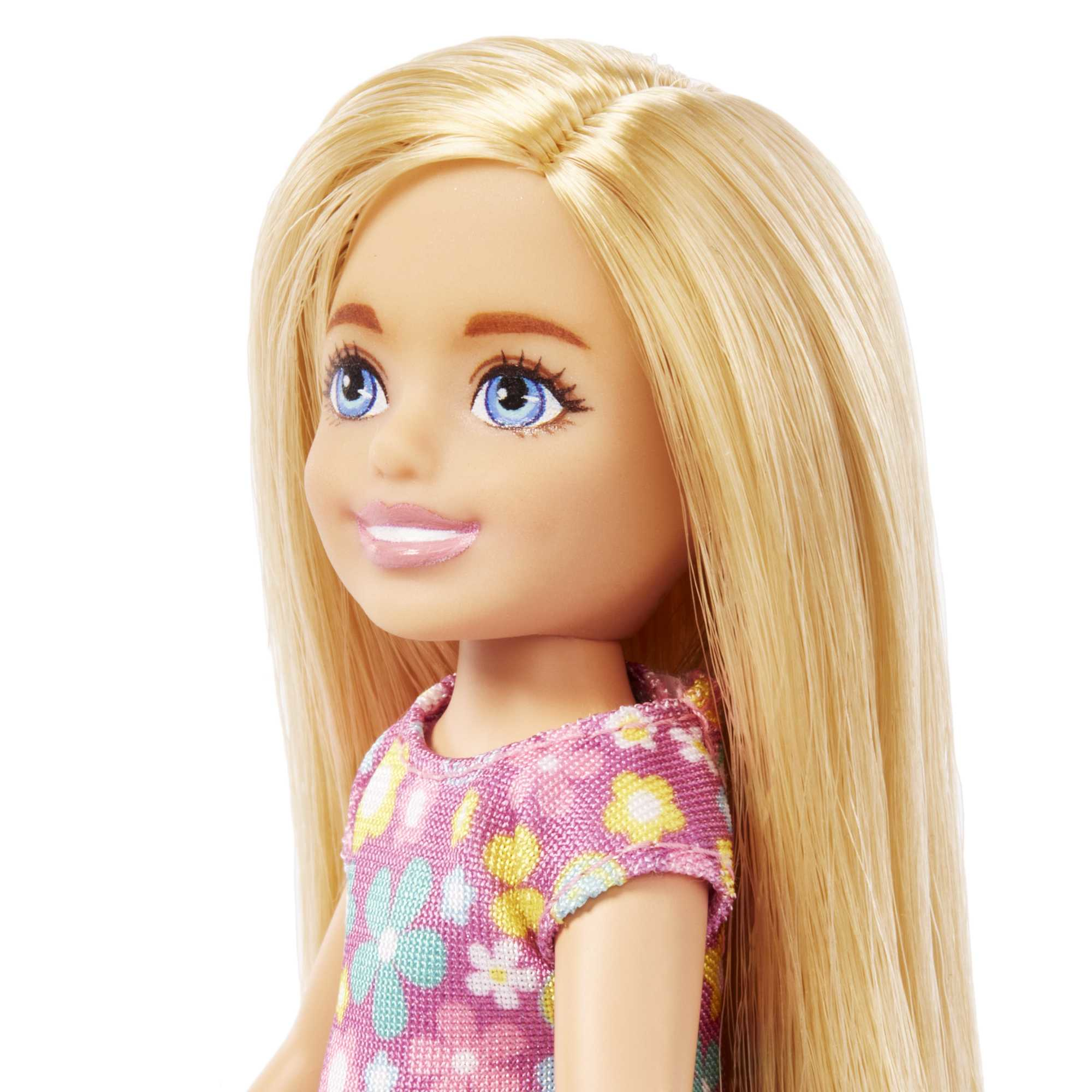 Gesicht einer blonden Puppe, lächelnd, blaue Augen, rosa Kleid mit Blumendruck, weißer Hintergrund.