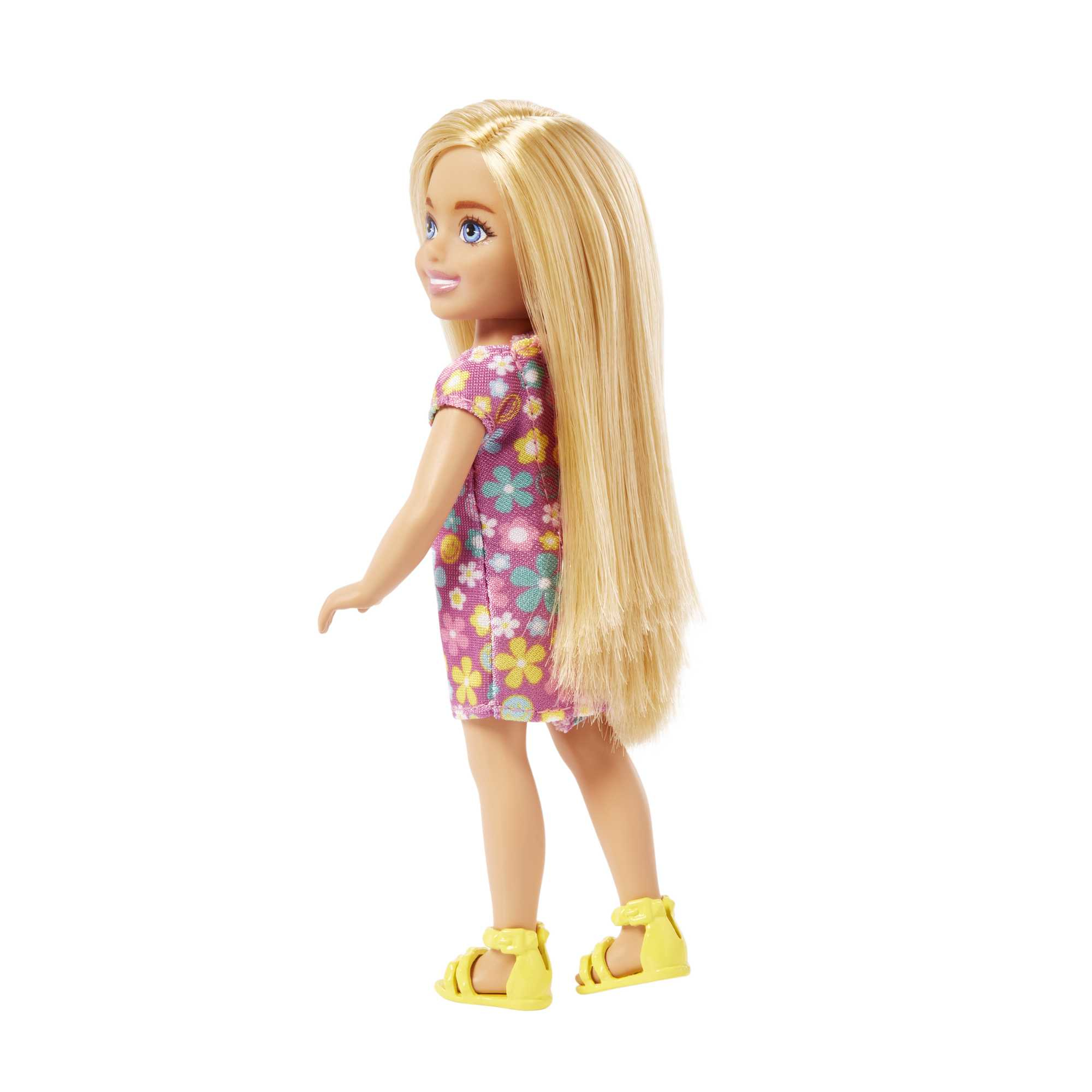 Blonde Puppe in einem Blumenkleid und gelben Sandalen, die zurückschaut. Weißer Hintergrund.