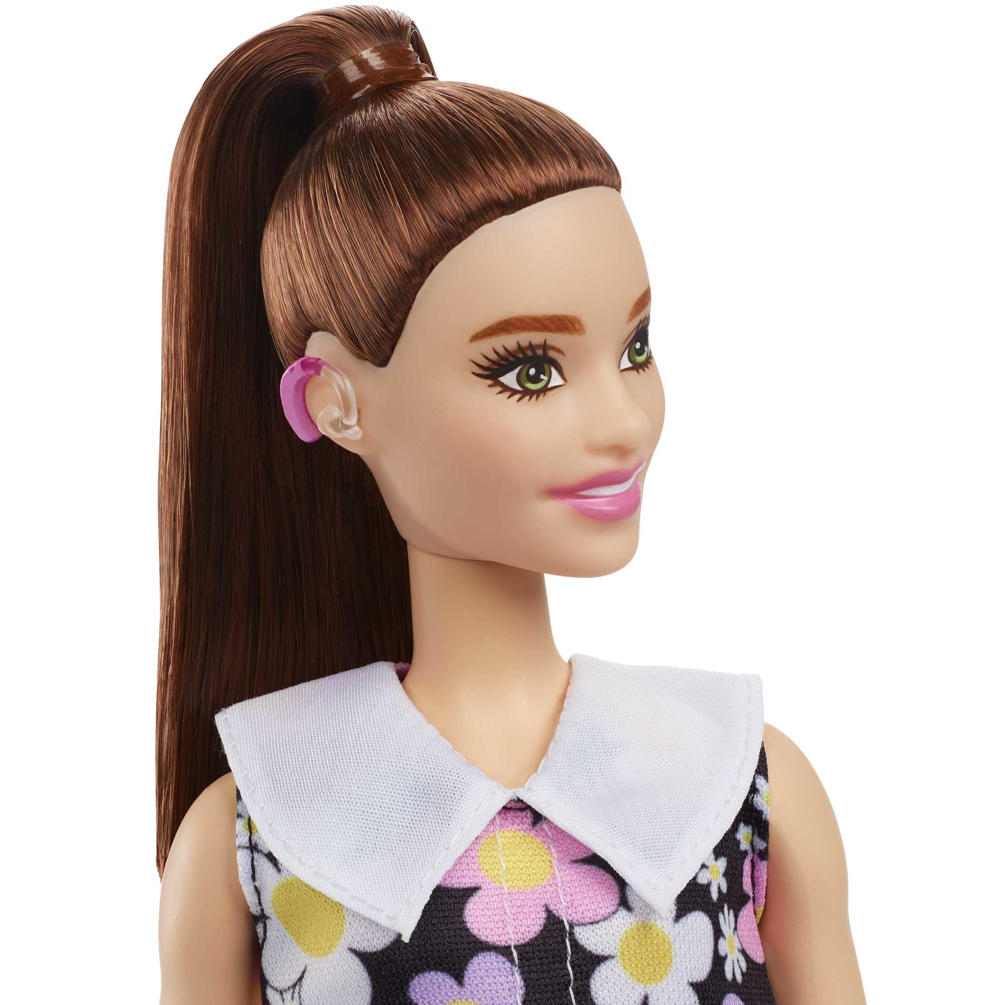 Barbie-Puppe mit braunen Haaren im Pferdeschwanz, trägt ein Blumenkleid und ein Hörgerät.