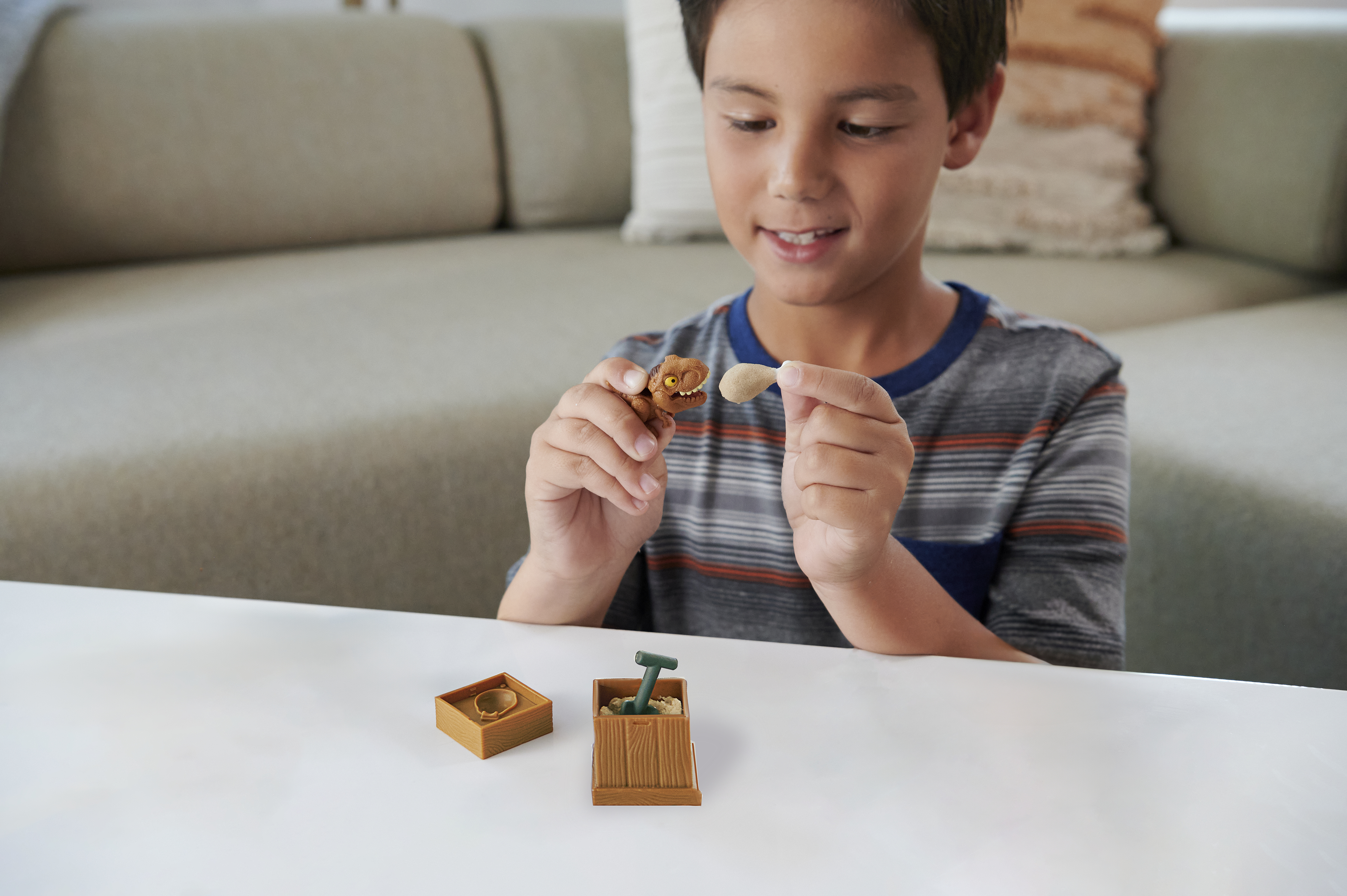Un niño pequeño sosteniendo y examinando pequeños fósiles de juguete. Hay una caja de madera y una pala.