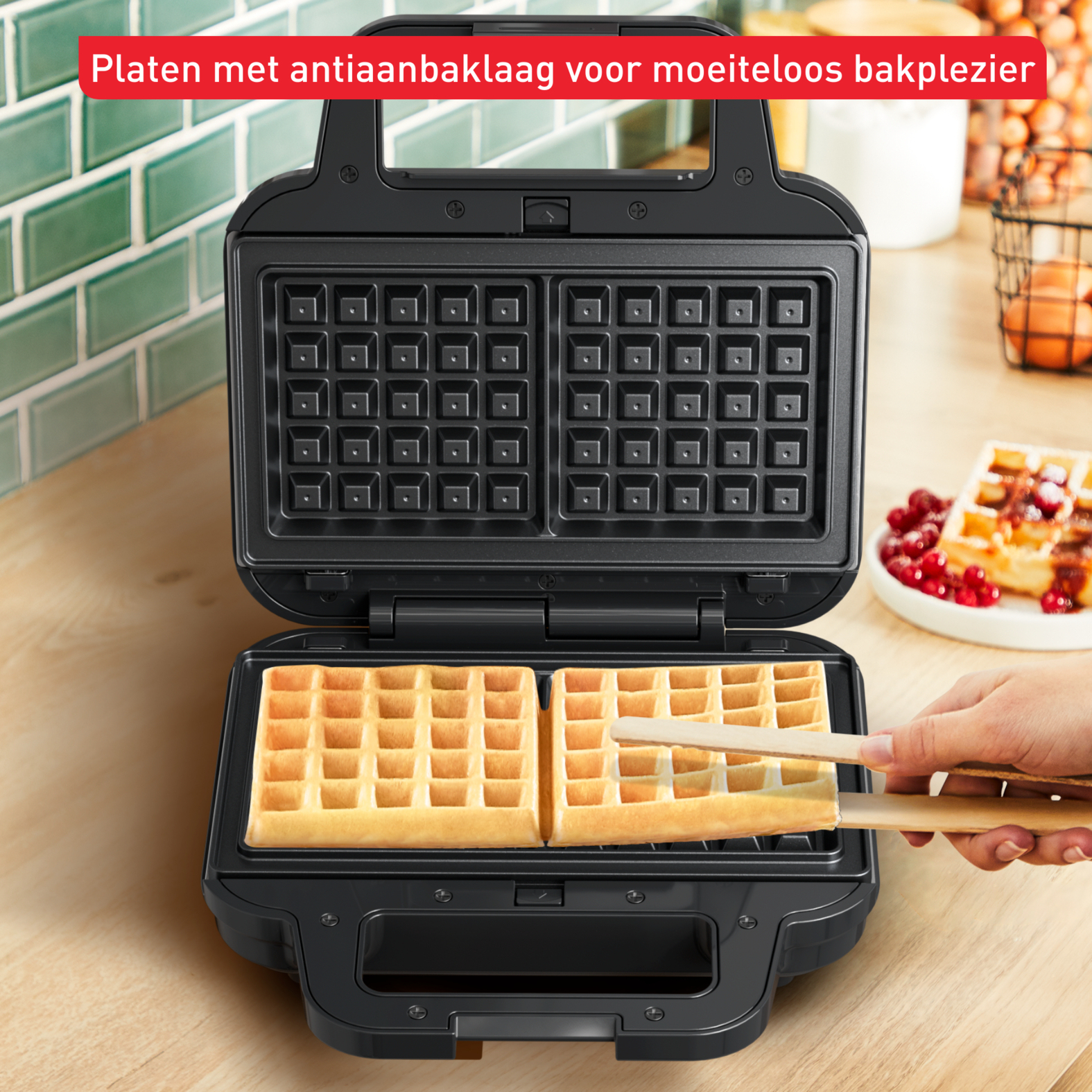 An open black waffle maker with two waffles inside. A hand is using tongs to remove one.