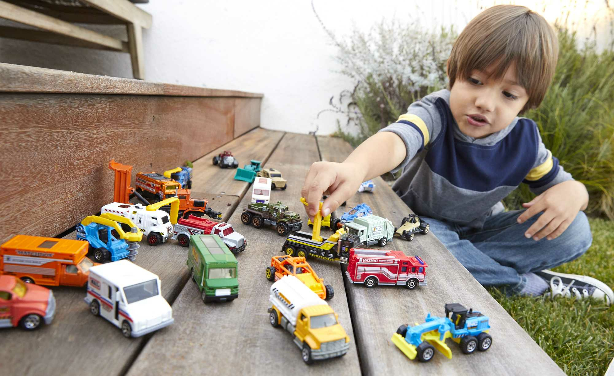 Un niño jugando con coches de juguete en una superficie de madera, con otros juguetes.
