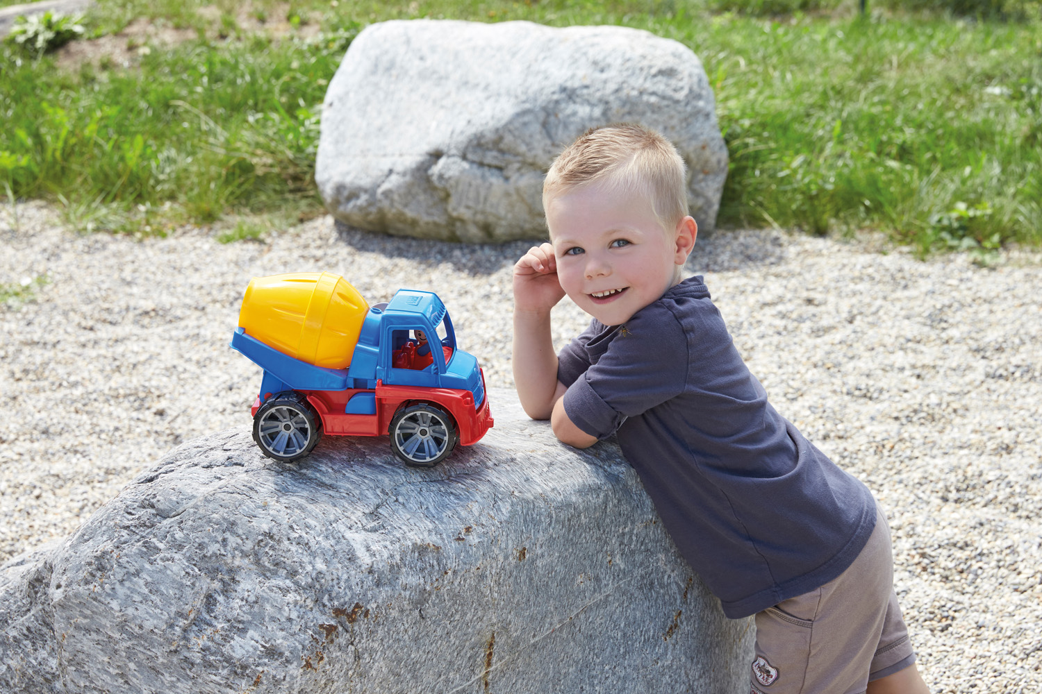 Ein Kind lehnt an einem Felsen neben einem Spielzeug-Zementmischer-LKW.